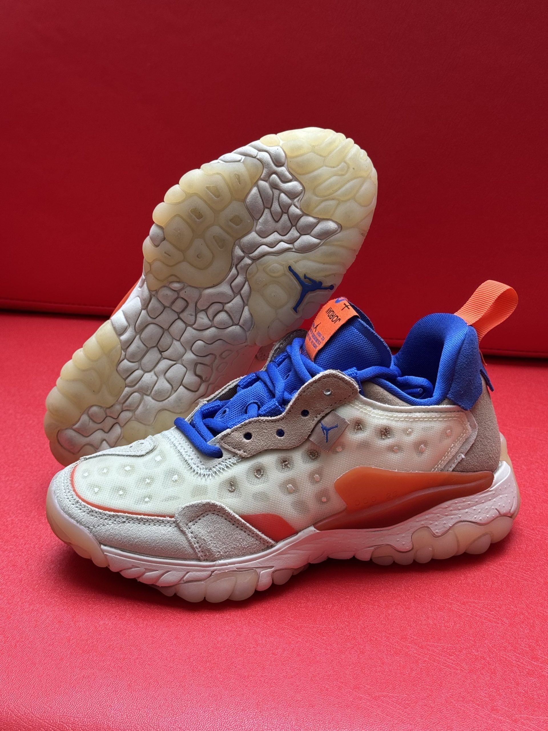 Beige, blue, and orange athletic shoe with visible sole tread on a red surface.