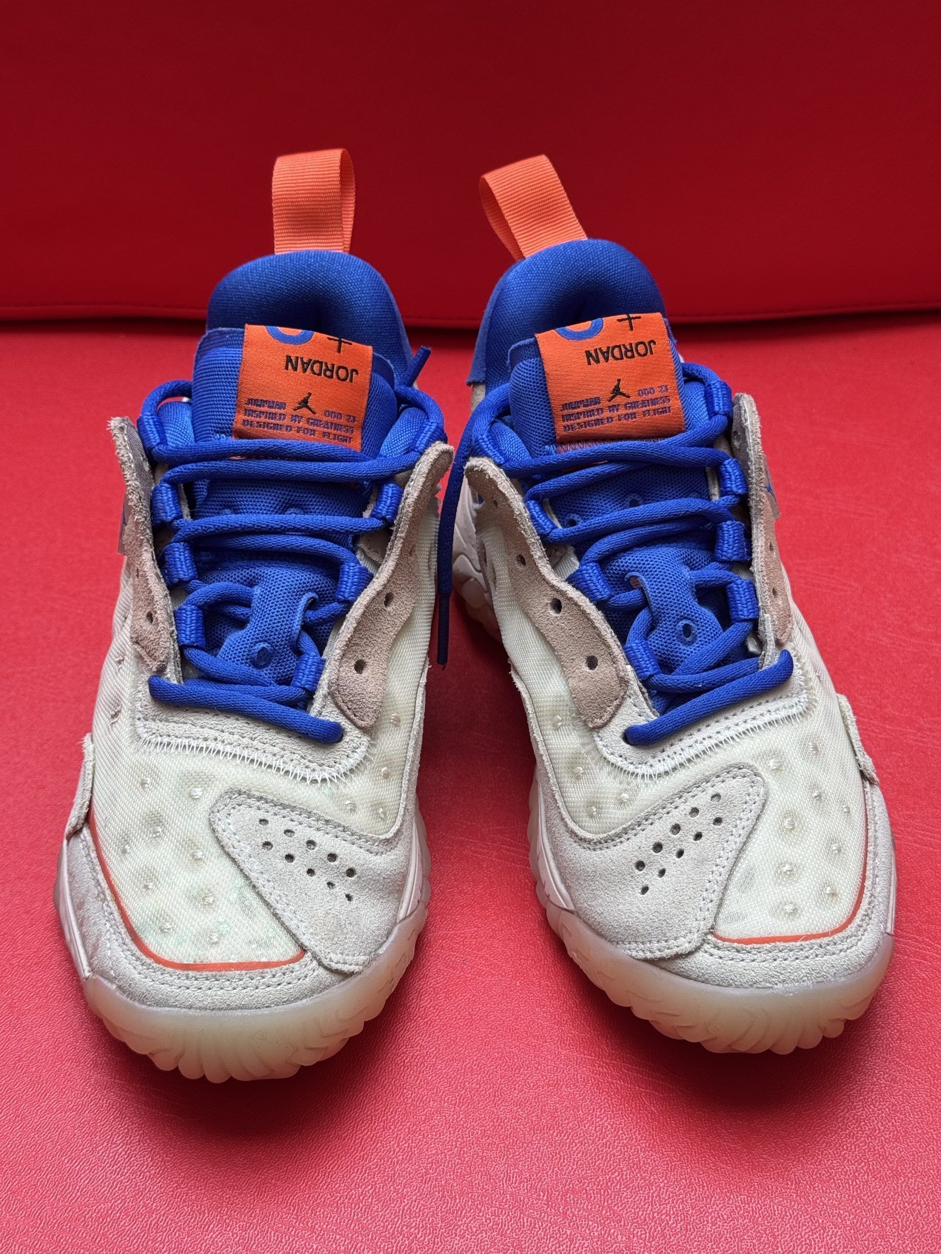 Beige, blue, and orange athletic shoe with visible sole tread on a red surface.