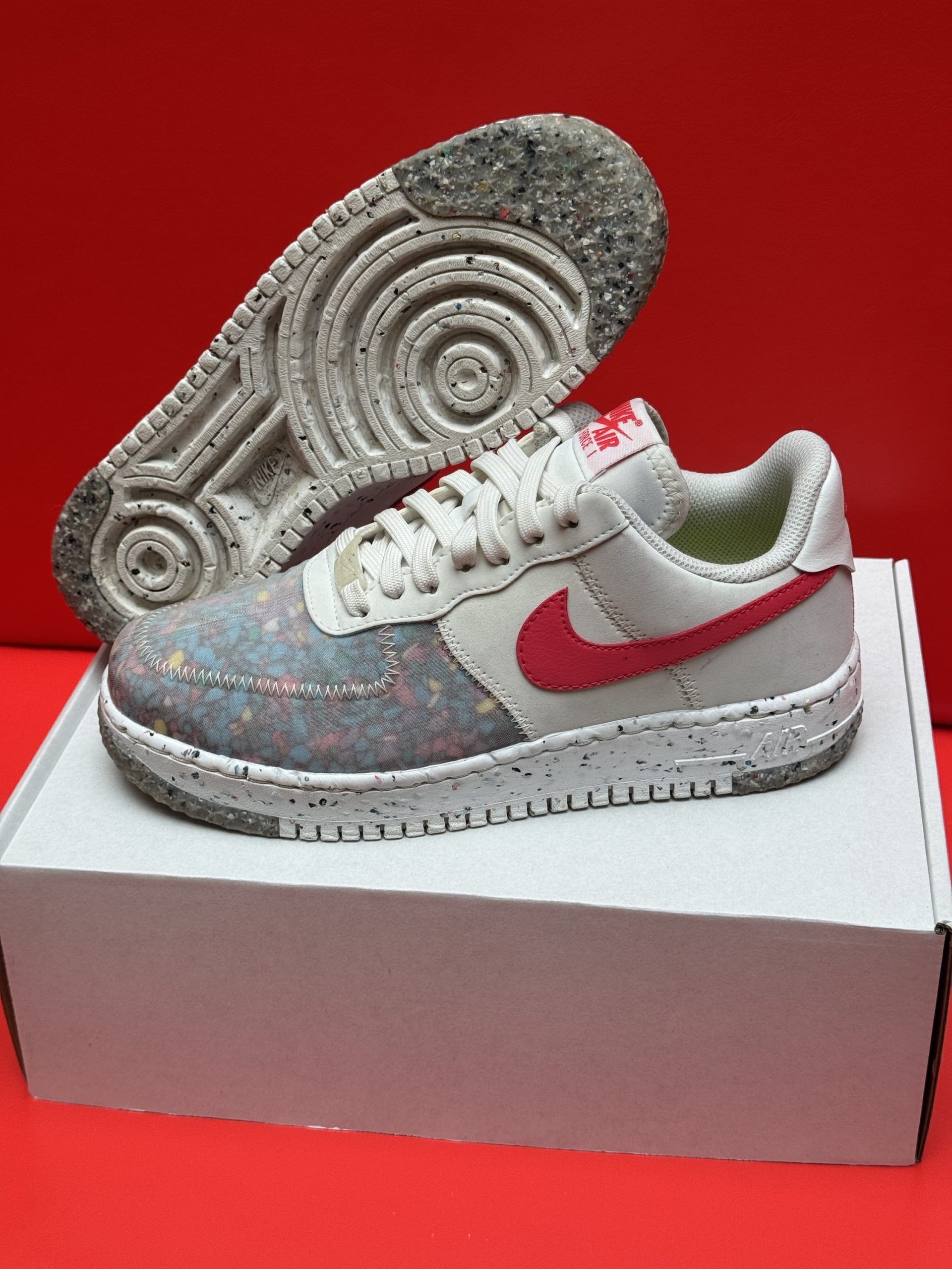 Nike Air Force 1 sneaker with a red swoosh, on a white box, red background.