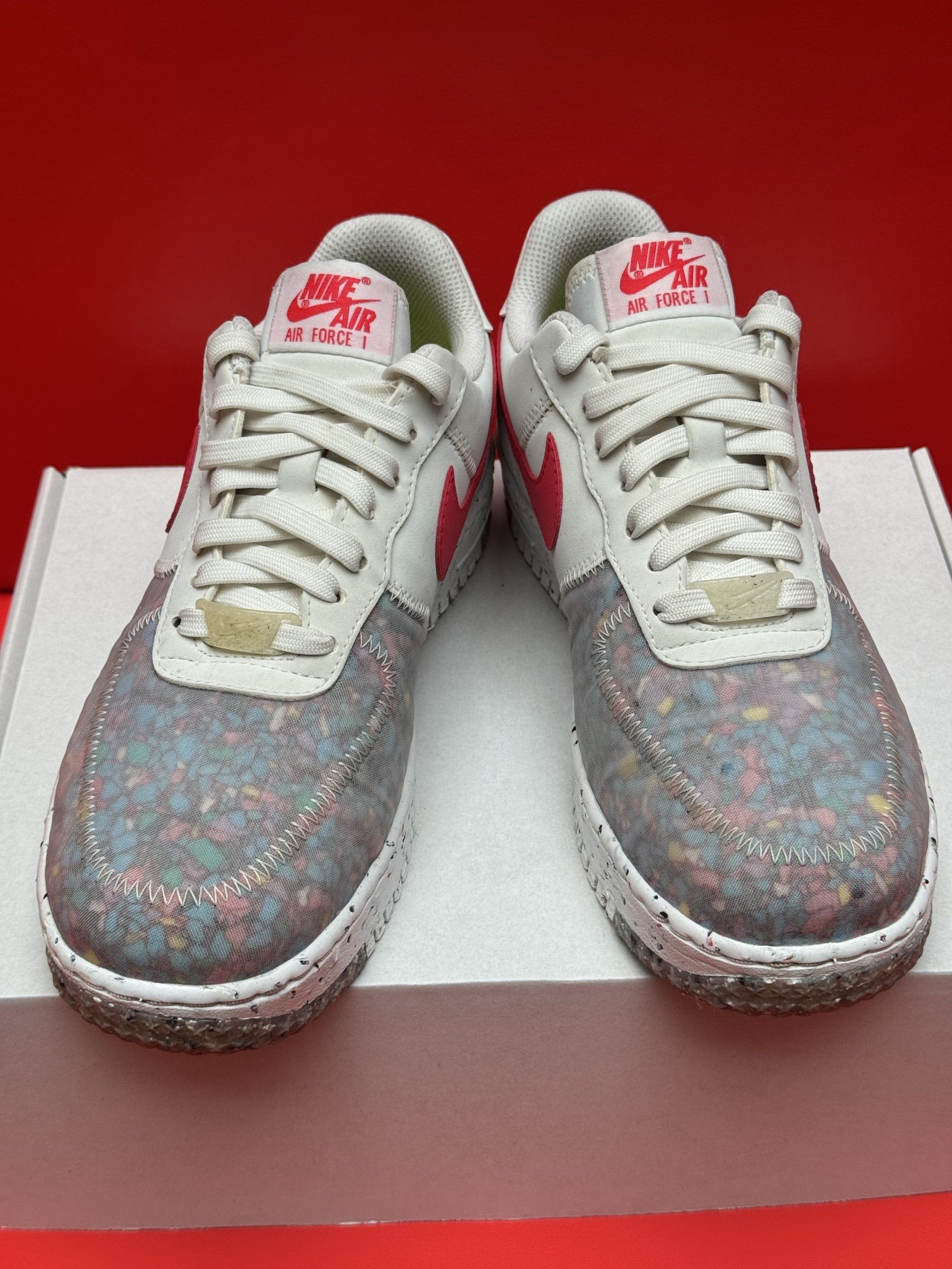 Nike Air Force 1 sneaker with a red swoosh, on a white box, red background.