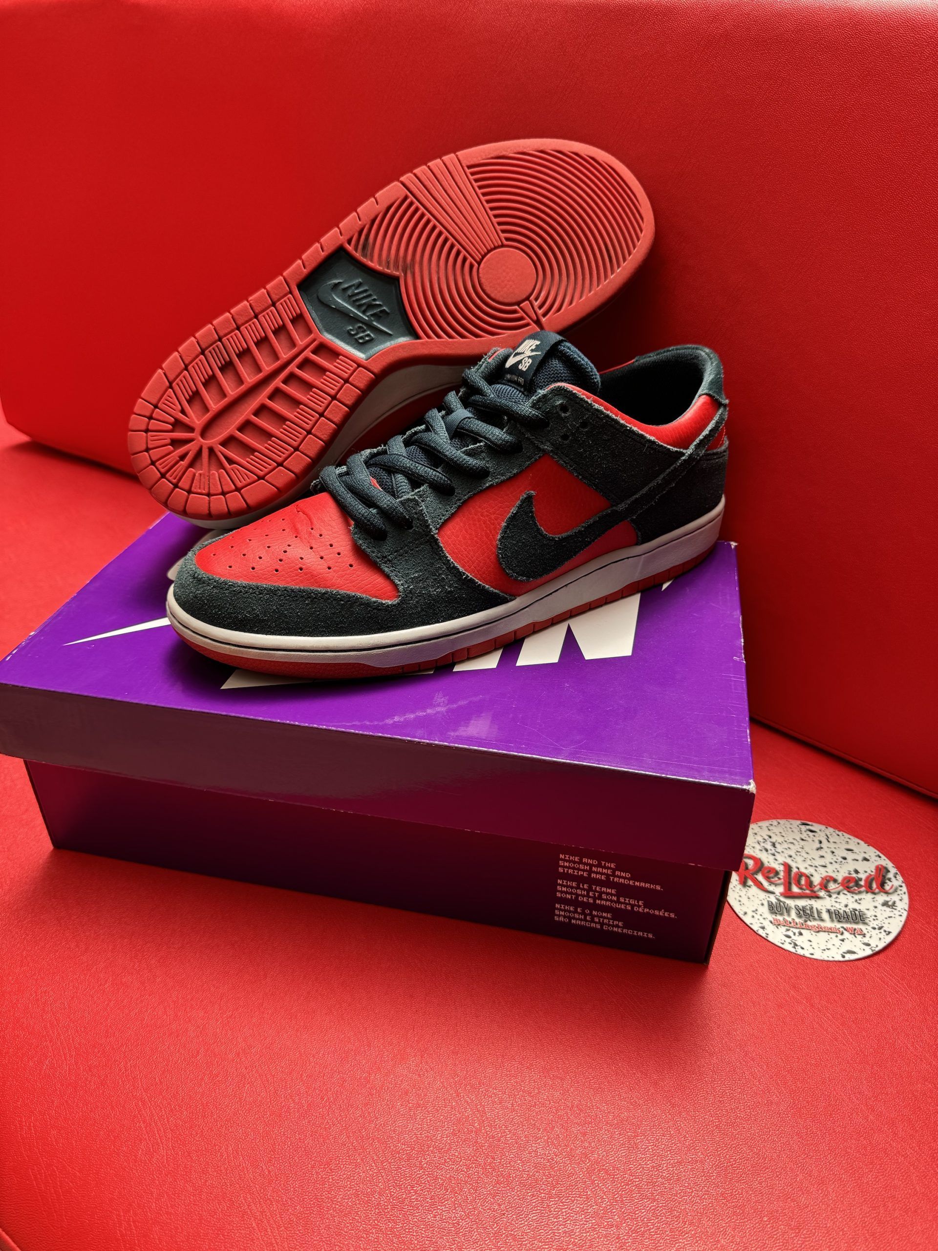 Red and black Nike Dunk SB sneakers on a purple box, one shoe upside down showing red sole.