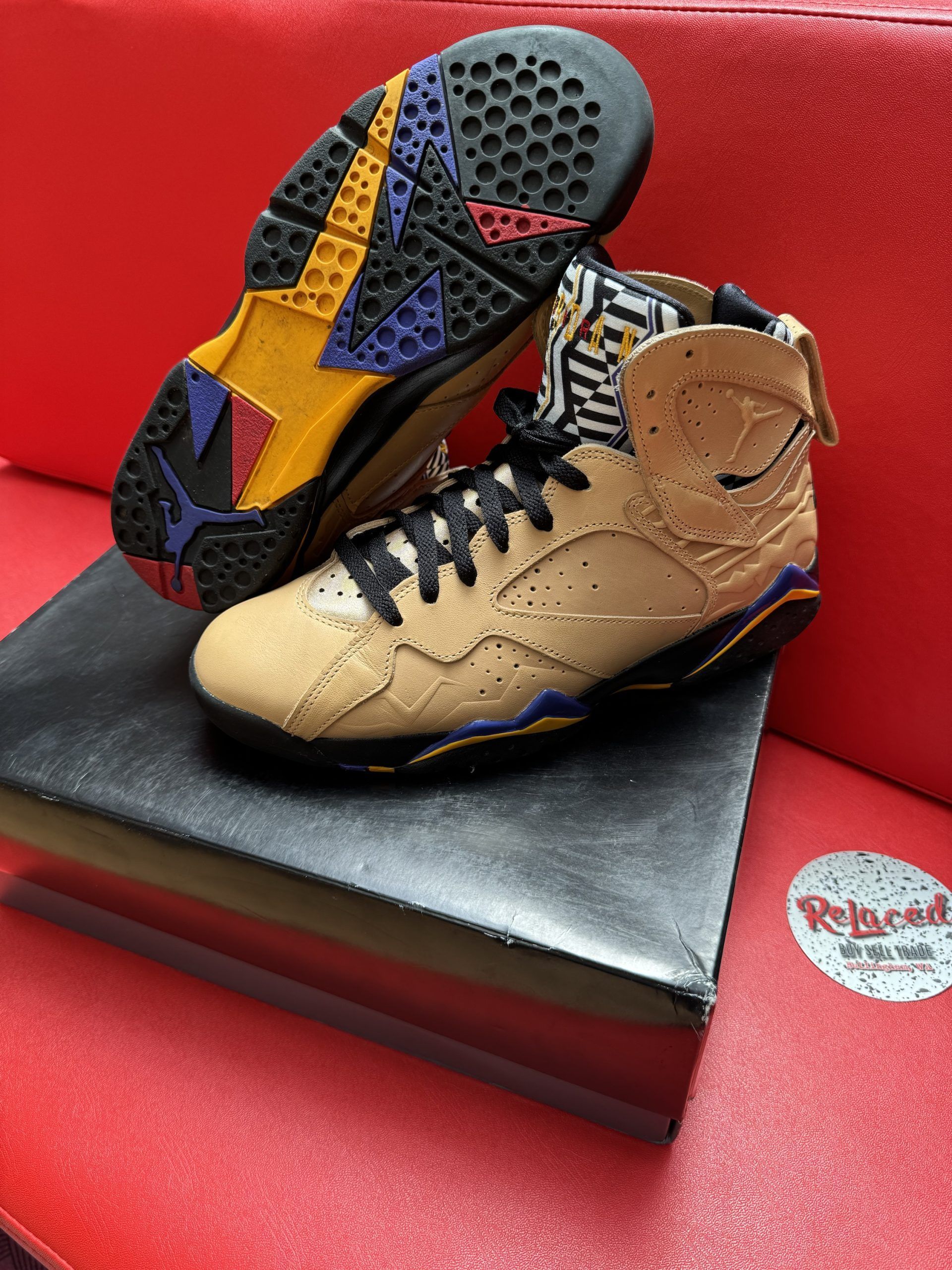 Tan and black Air Jordan 7 sneakers on a black box, sole visible.
