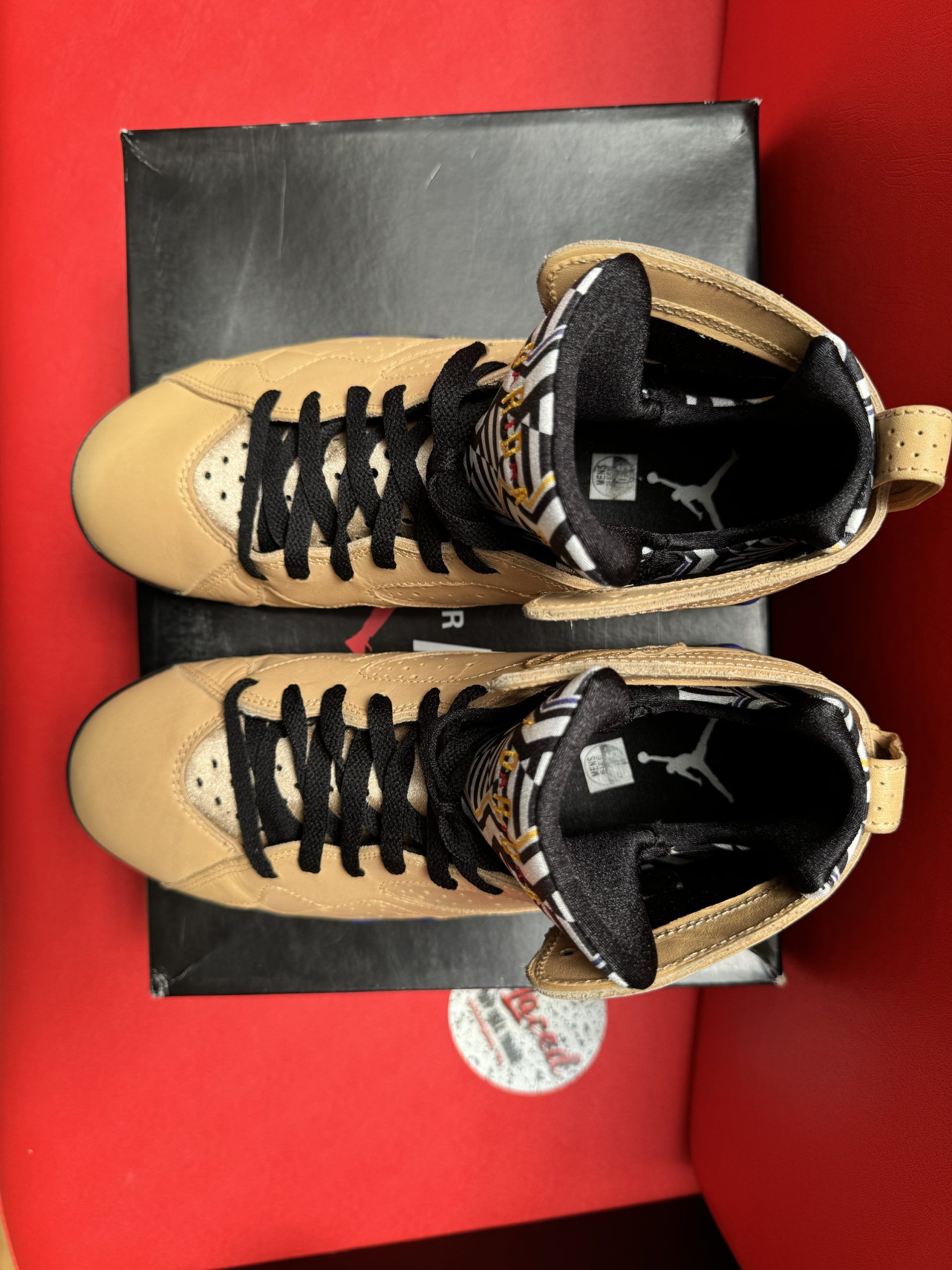 Tan and black Air Jordan 7 sneakers on a black box, sole visible.