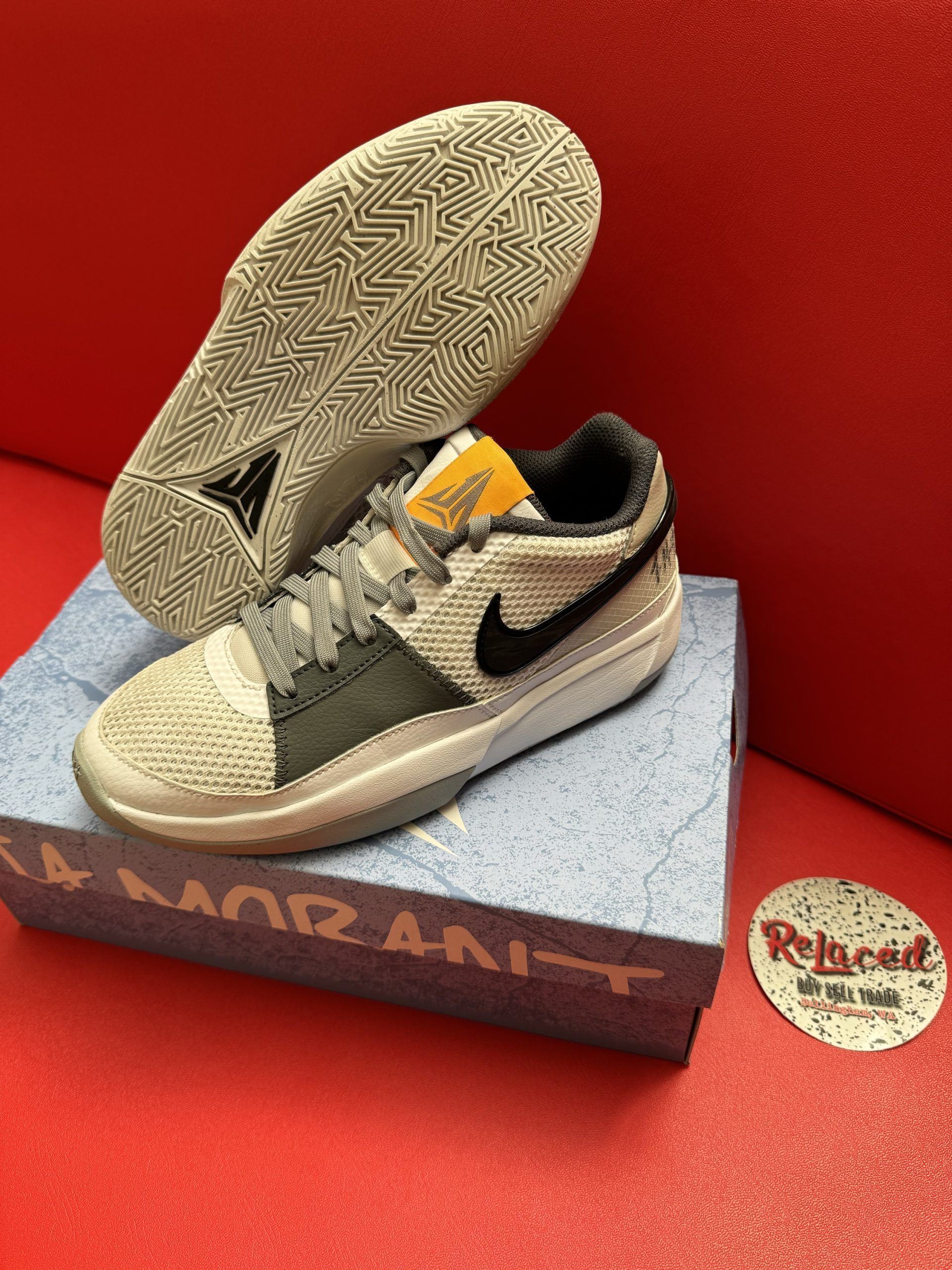 Gray and white Nike Ja 1 sneakers on a box, sole up. Black swoosh, orange tag.