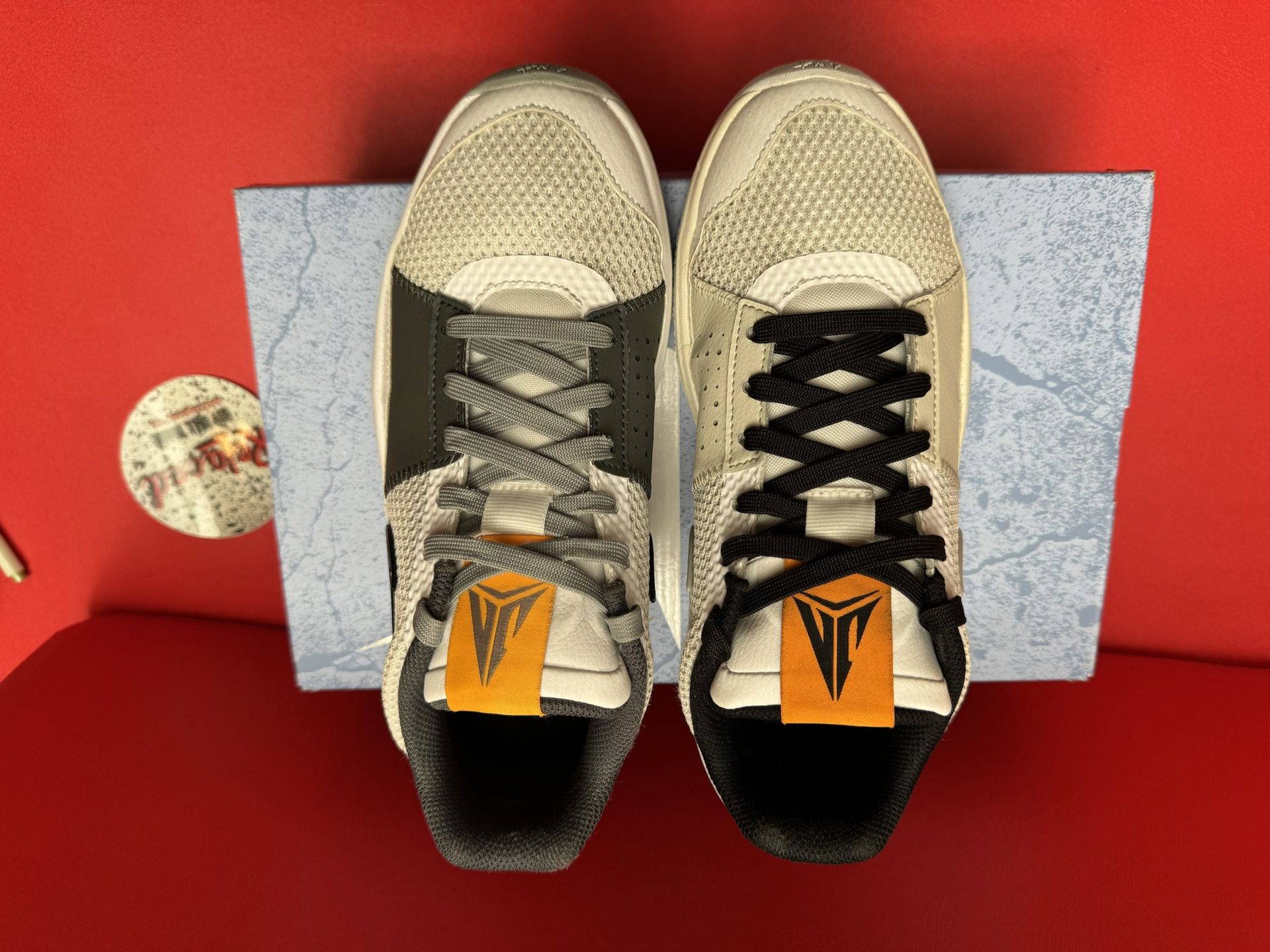 Gray and white Nike Ja 1 sneakers on a box, sole up. Black swoosh, orange tag.