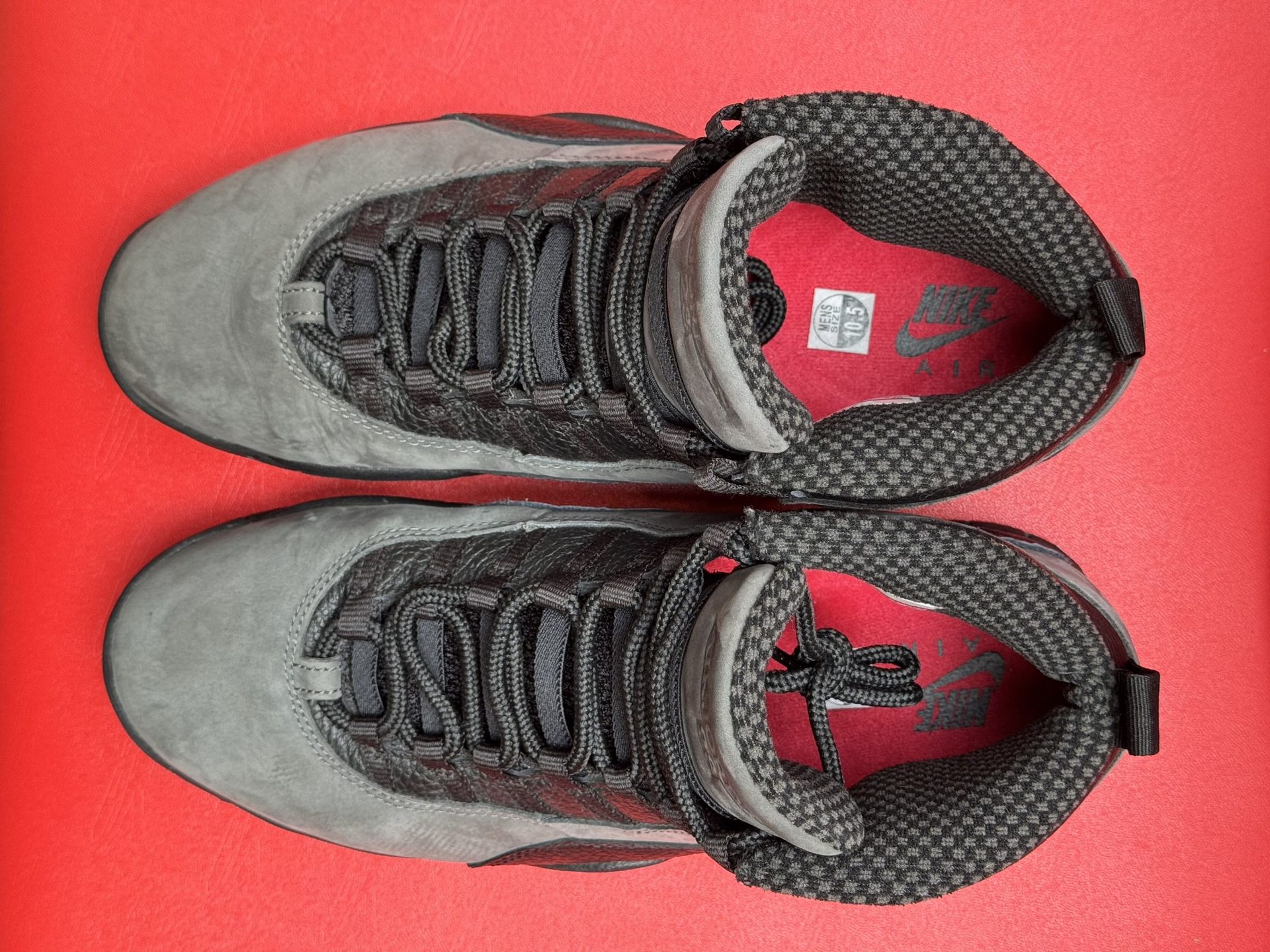 Gray and black Air Jordan 10 sneakers on a red surface. Sole is visible with red Jumpman logo.