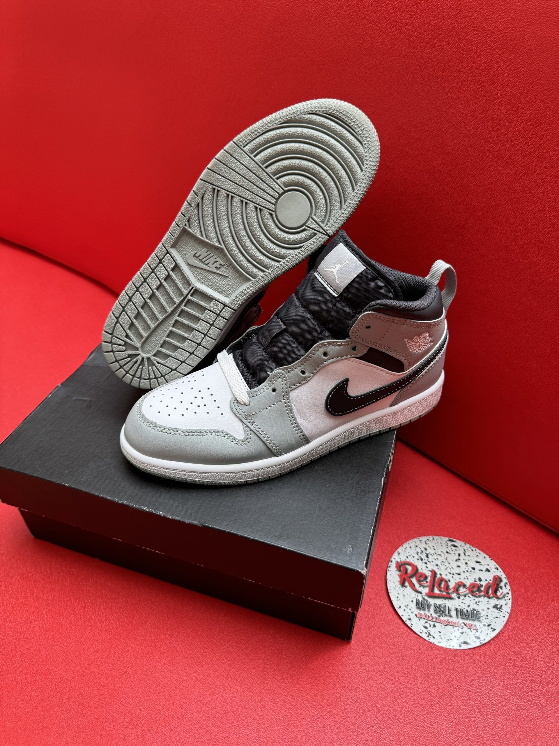 Gray, white, and black Air Jordan 1 sneaker on a black box, sole visible.