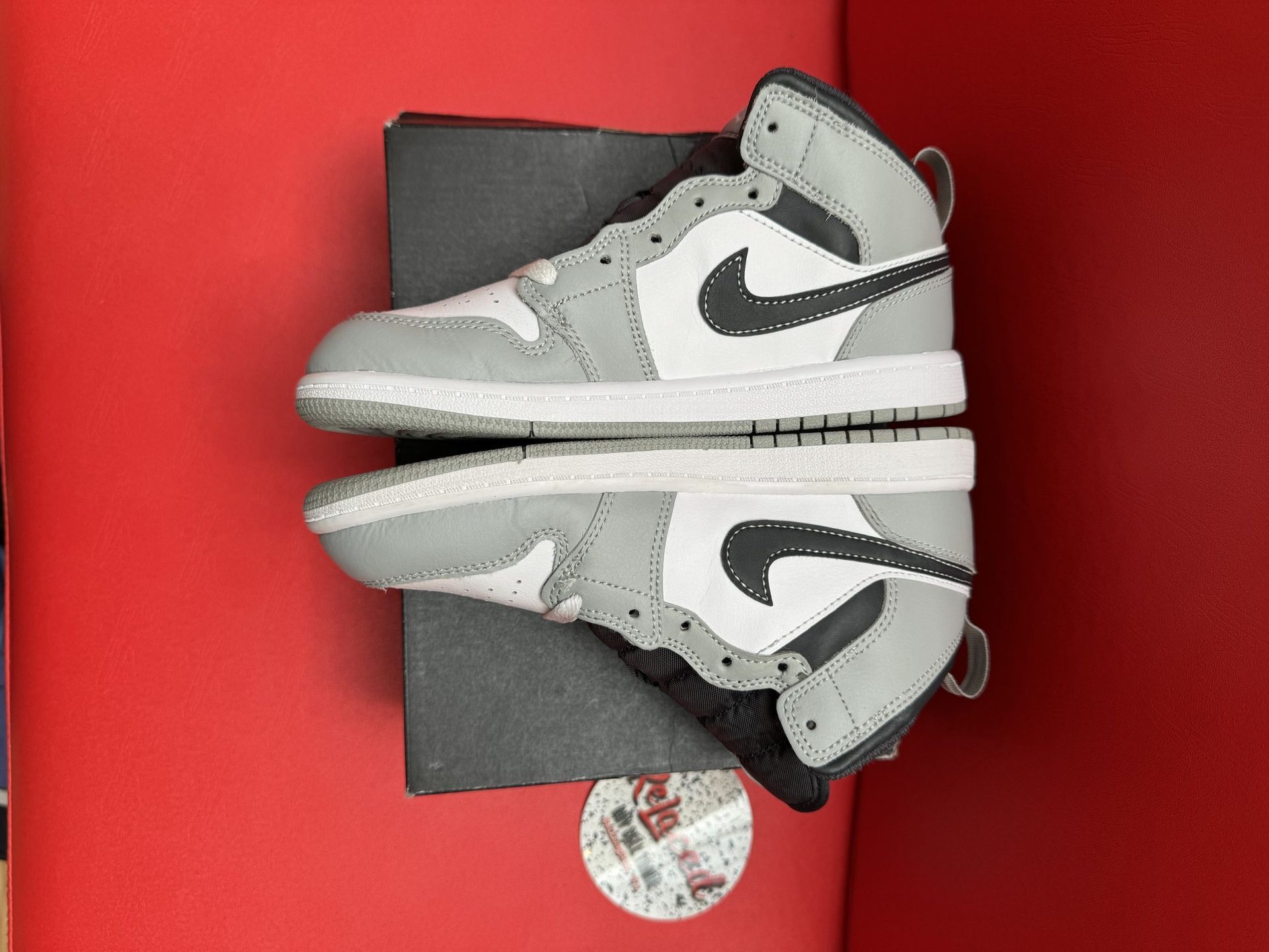 Gray, white, and black Air Jordan 1 sneaker on a black box, sole visible.
