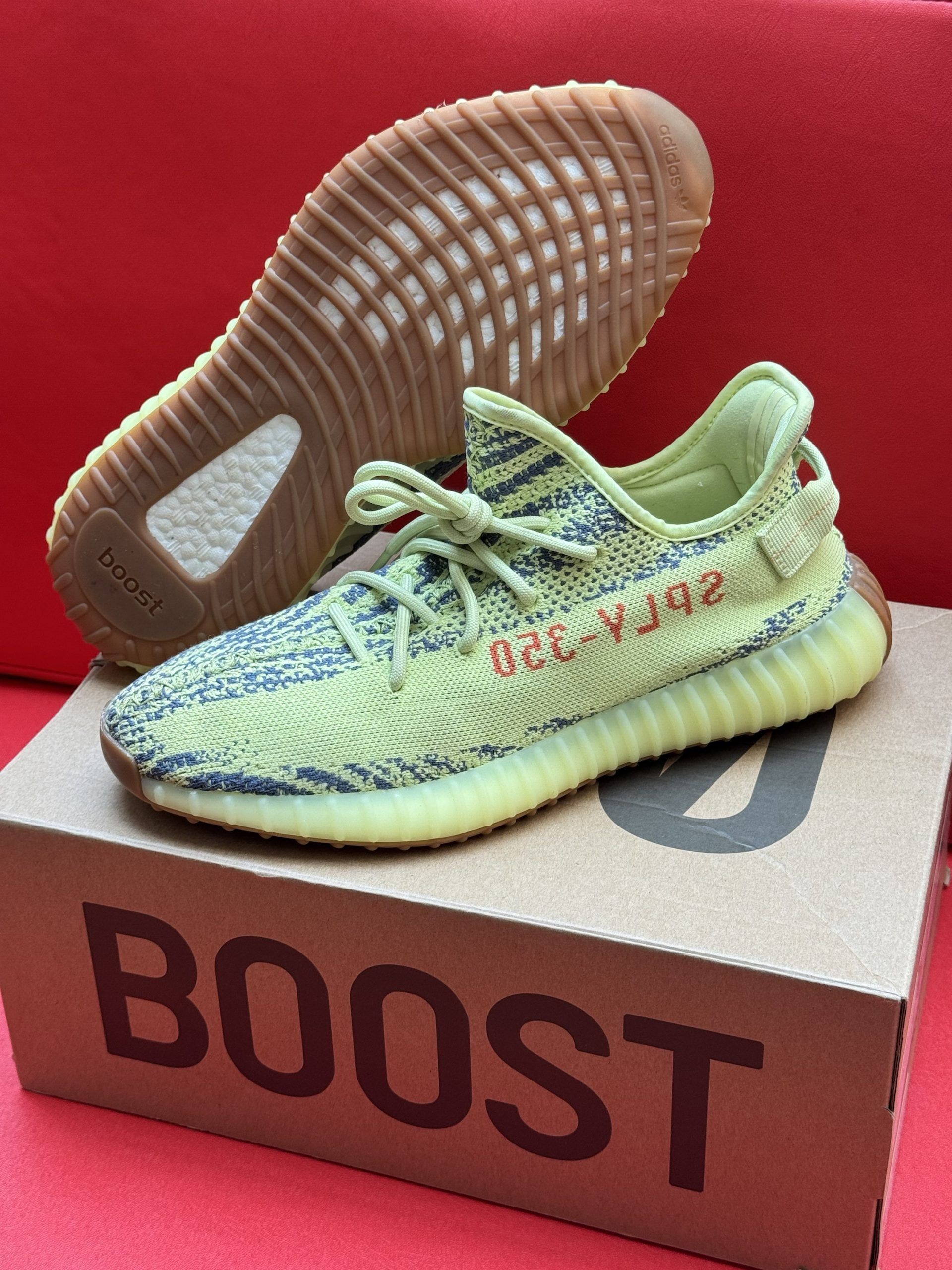 Yellow and blue Adidas Yeezy Boost 350 V2 sneakers on a cardboard box, with a red background.