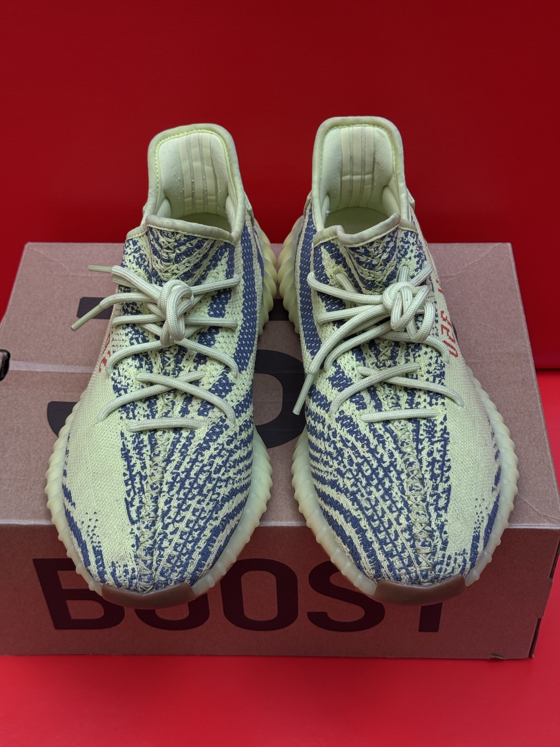 Yellow and blue Adidas Yeezy Boost 350 V2 sneakers on a cardboard box, with a red background.