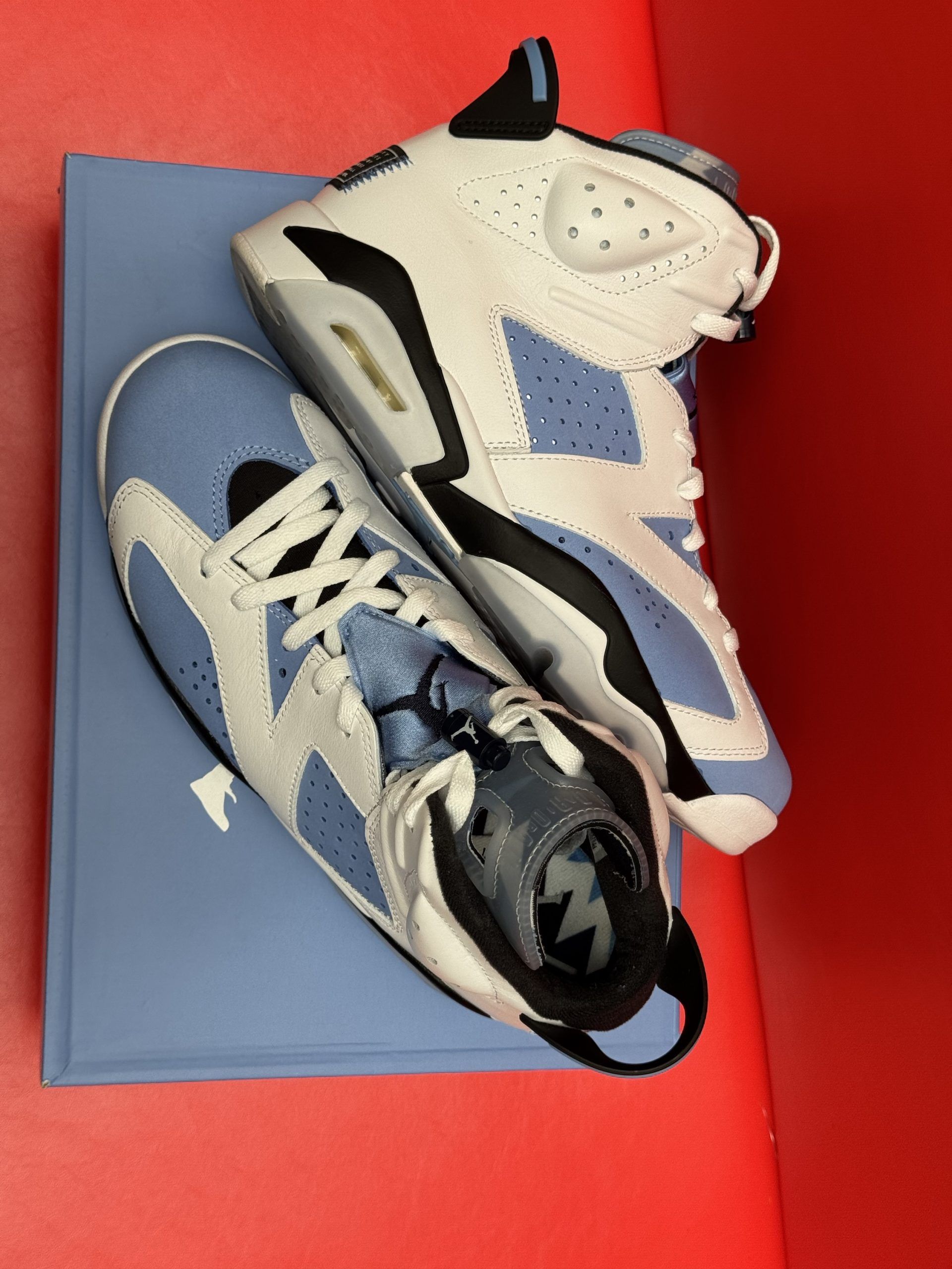 Air Jordan 6 sneakers in light blue and white, resting on a blue shoe box, with one sole visible.