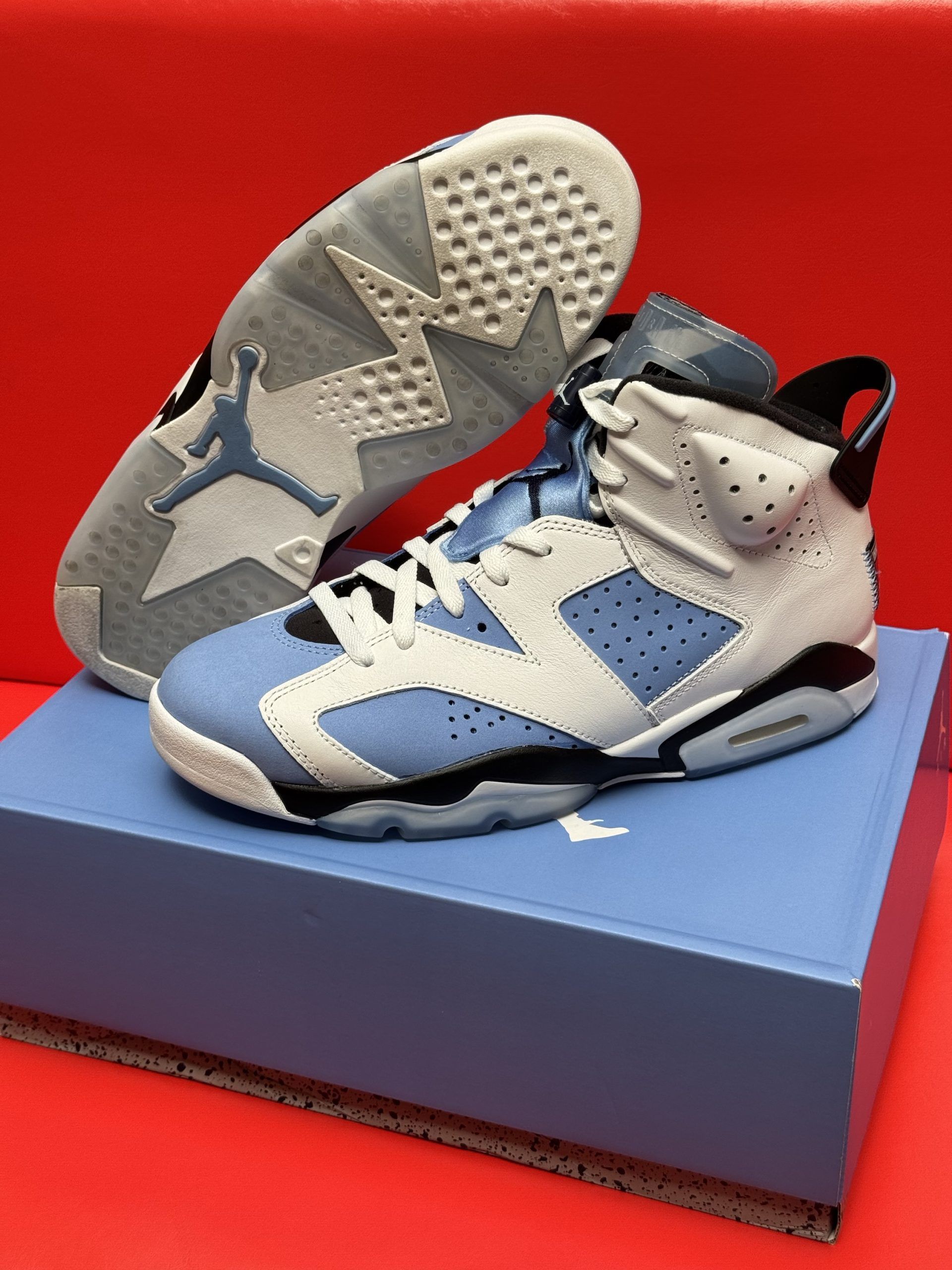Air Jordan 6 sneakers in light blue and white, resting on a blue shoe box, with one sole visible.