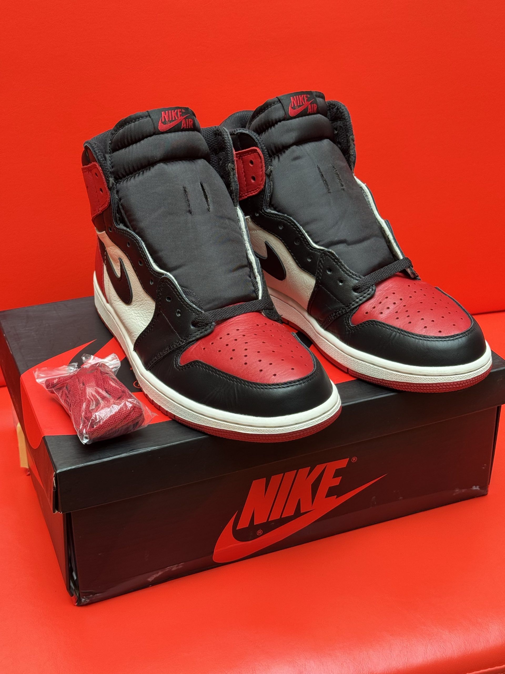 Air Jordan 1 sneakers in black, white, and red on a shoebox against a red background.