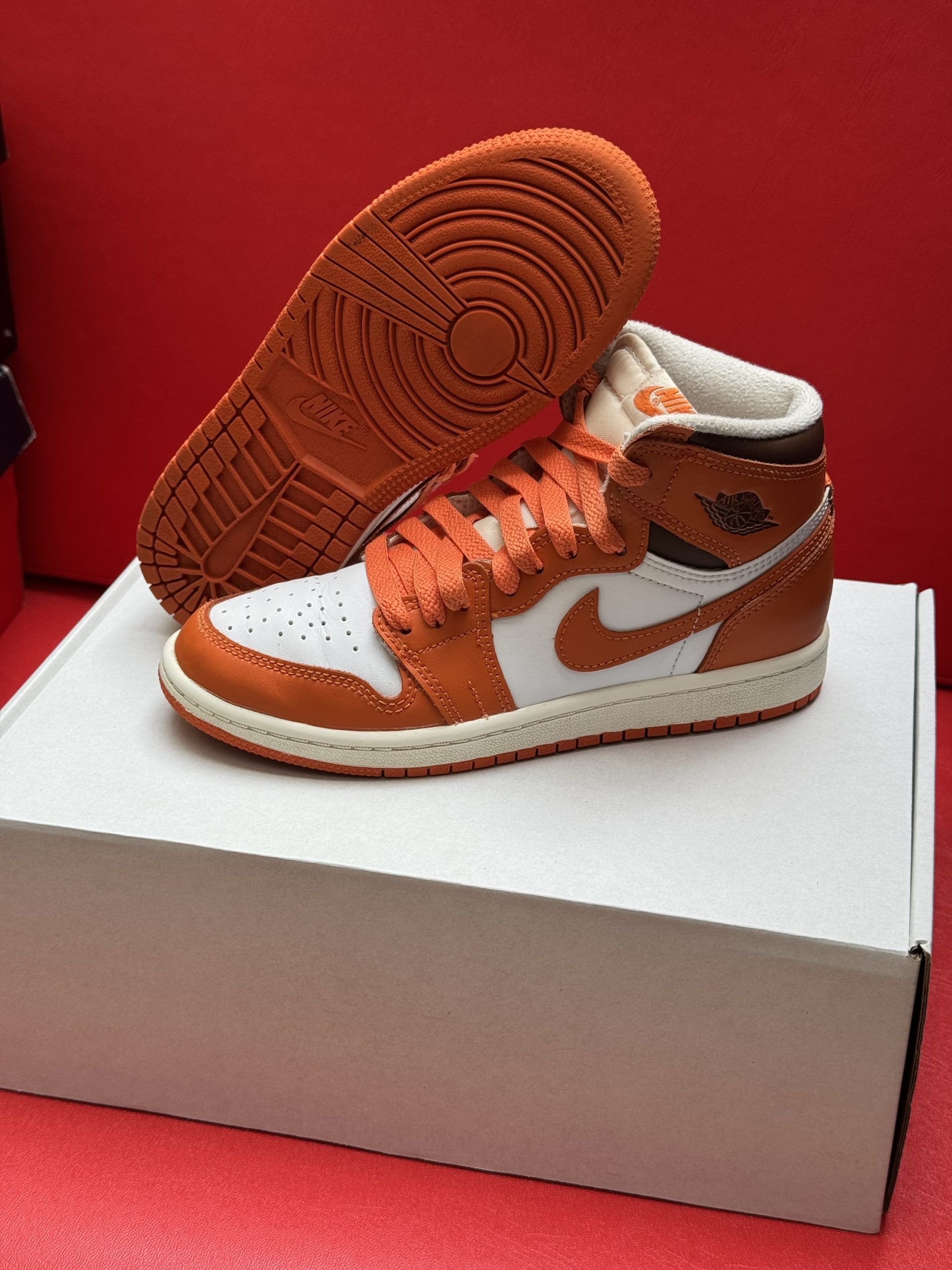 Orange and white Air Jordan 1 sneaker on a white box, with the orange sole visible.
