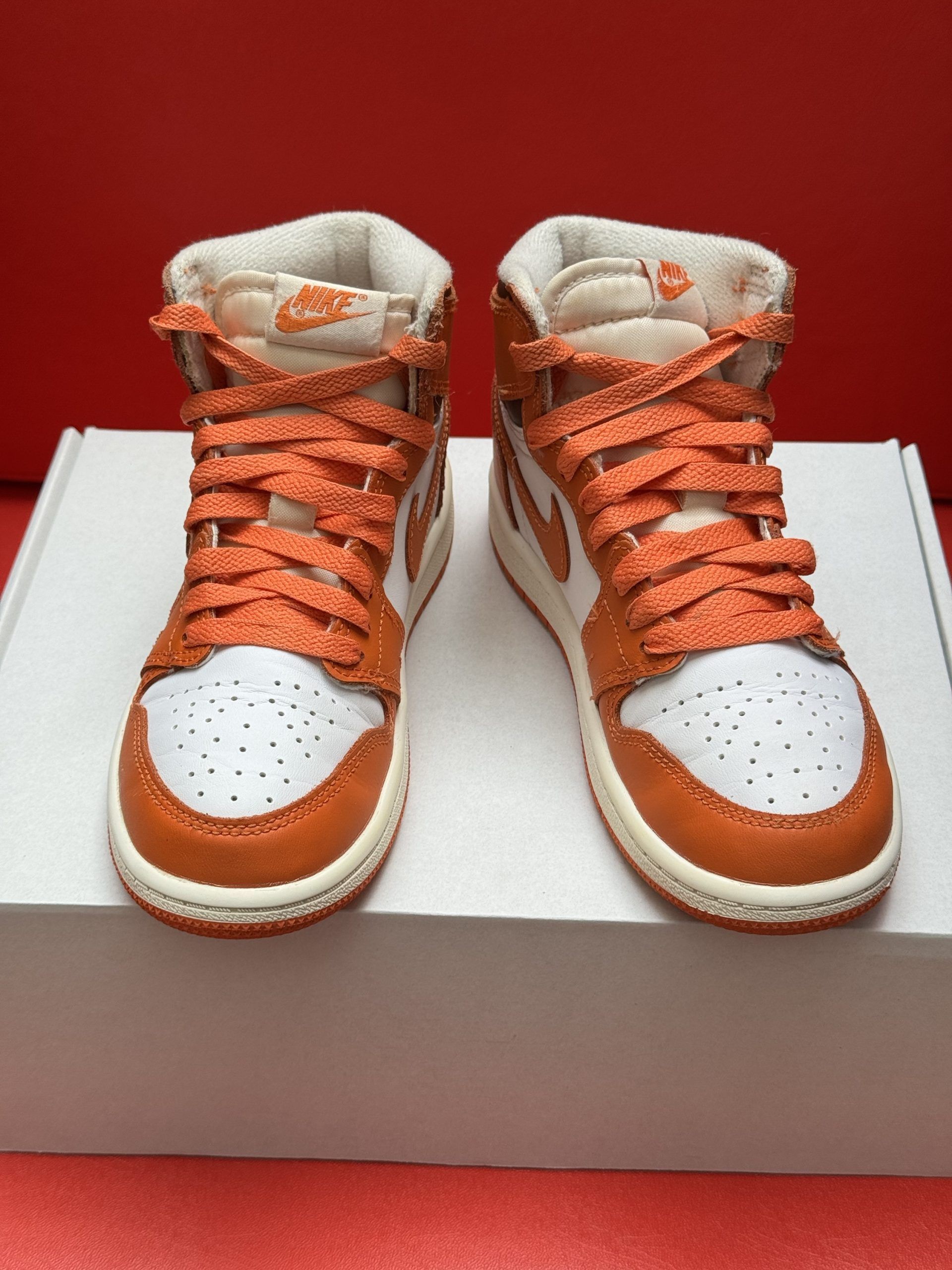Orange and white Air Jordan 1 sneaker on a white box, with the orange sole visible.