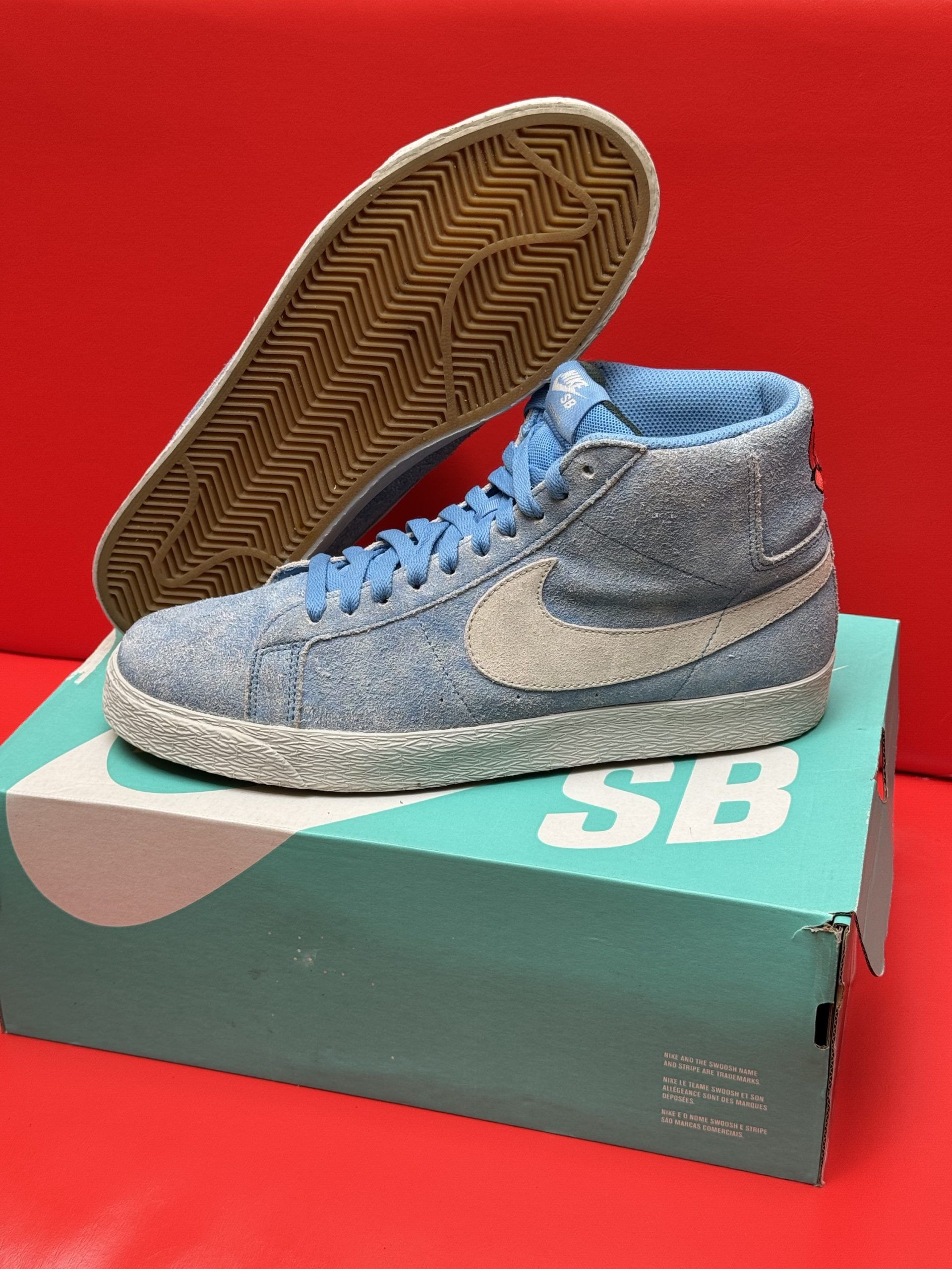 Light blue Nike SB Blazer high-top sneakers with a white swoosh, on a teal box.