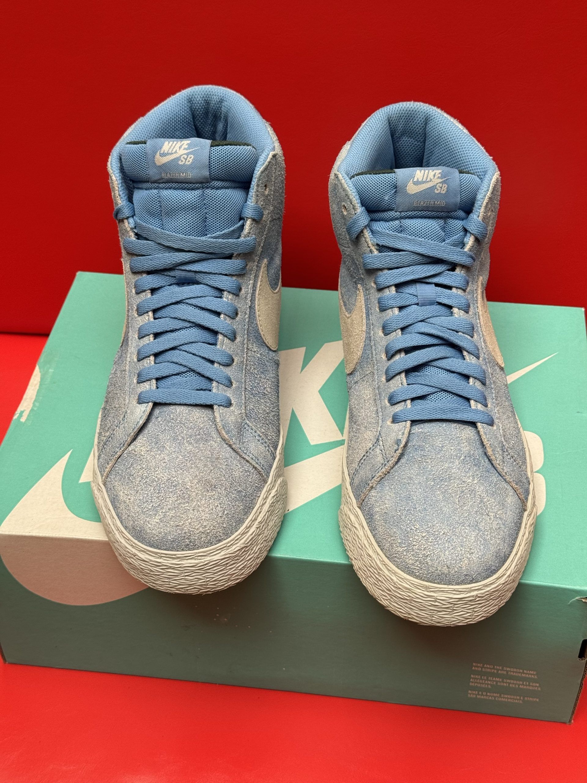 Light blue Nike SB Blazer high-top sneakers with a white swoosh, on a teal box.
