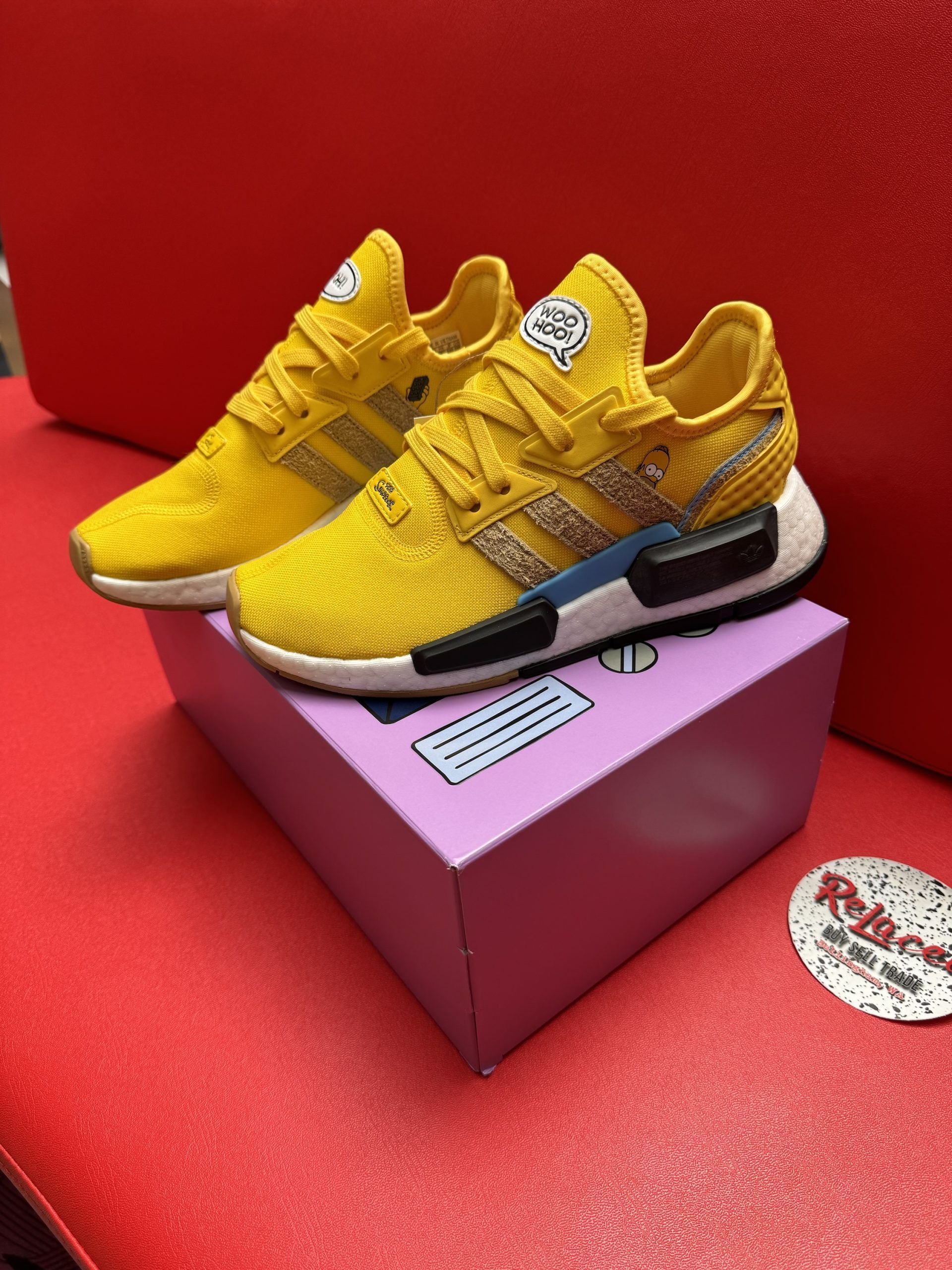 Yellow Adidas sneakers on a purple box with a TV design, set on a red surface.