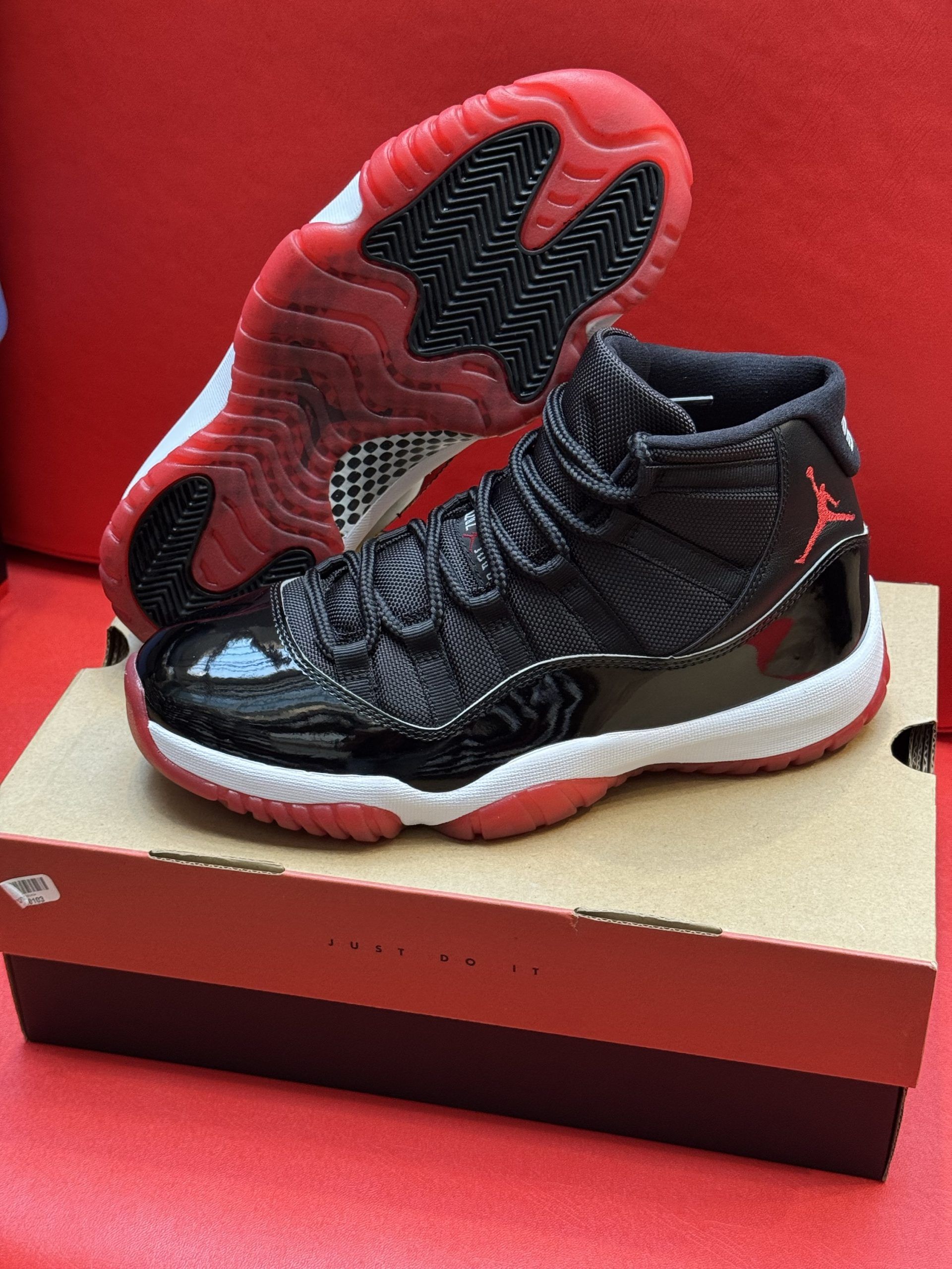 Black and red Air Jordan 11 sneakers on a cardboard box, with a red background.