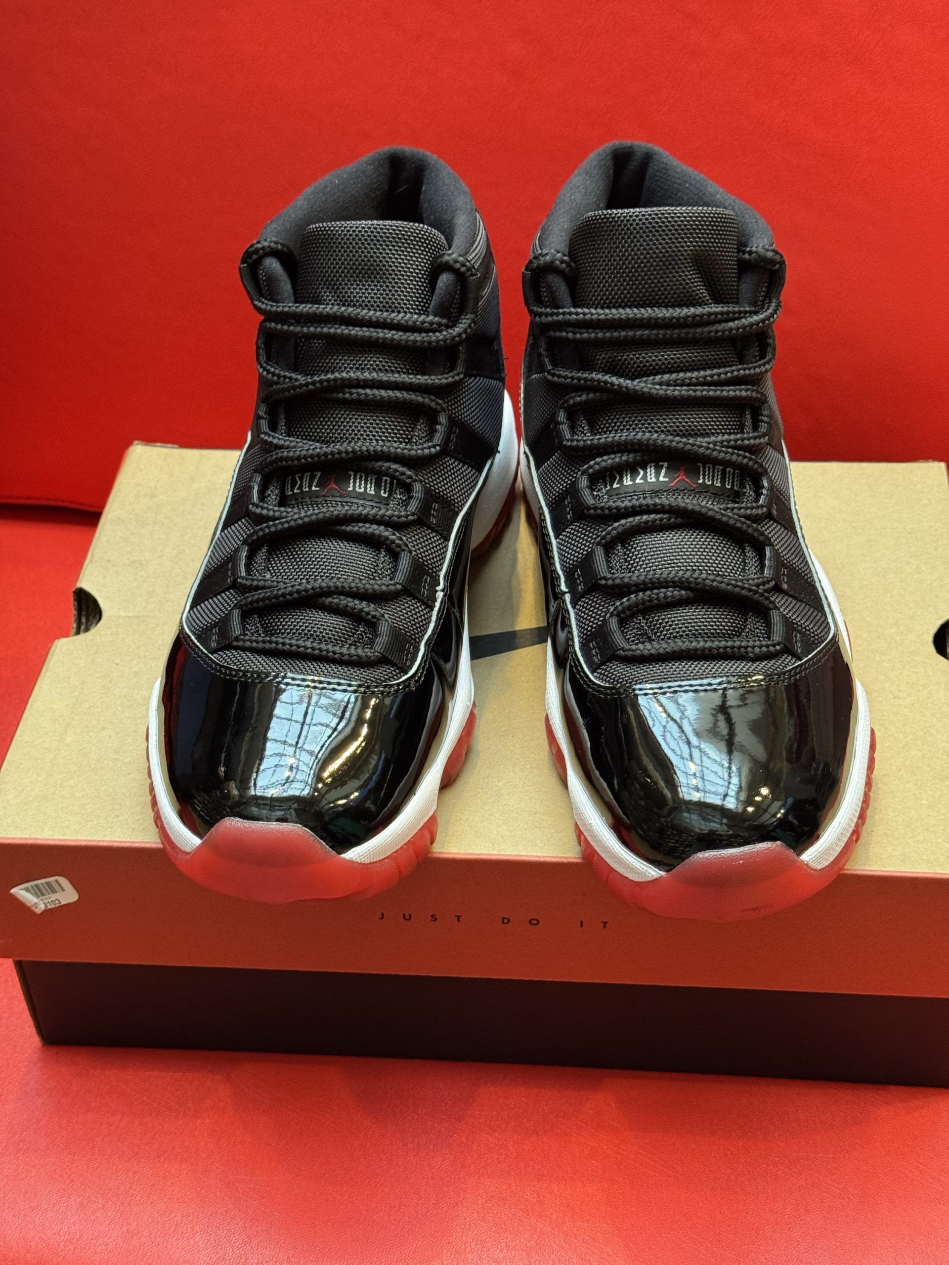 Black and red Air Jordan 11 sneakers on a cardboard box, with a red background.