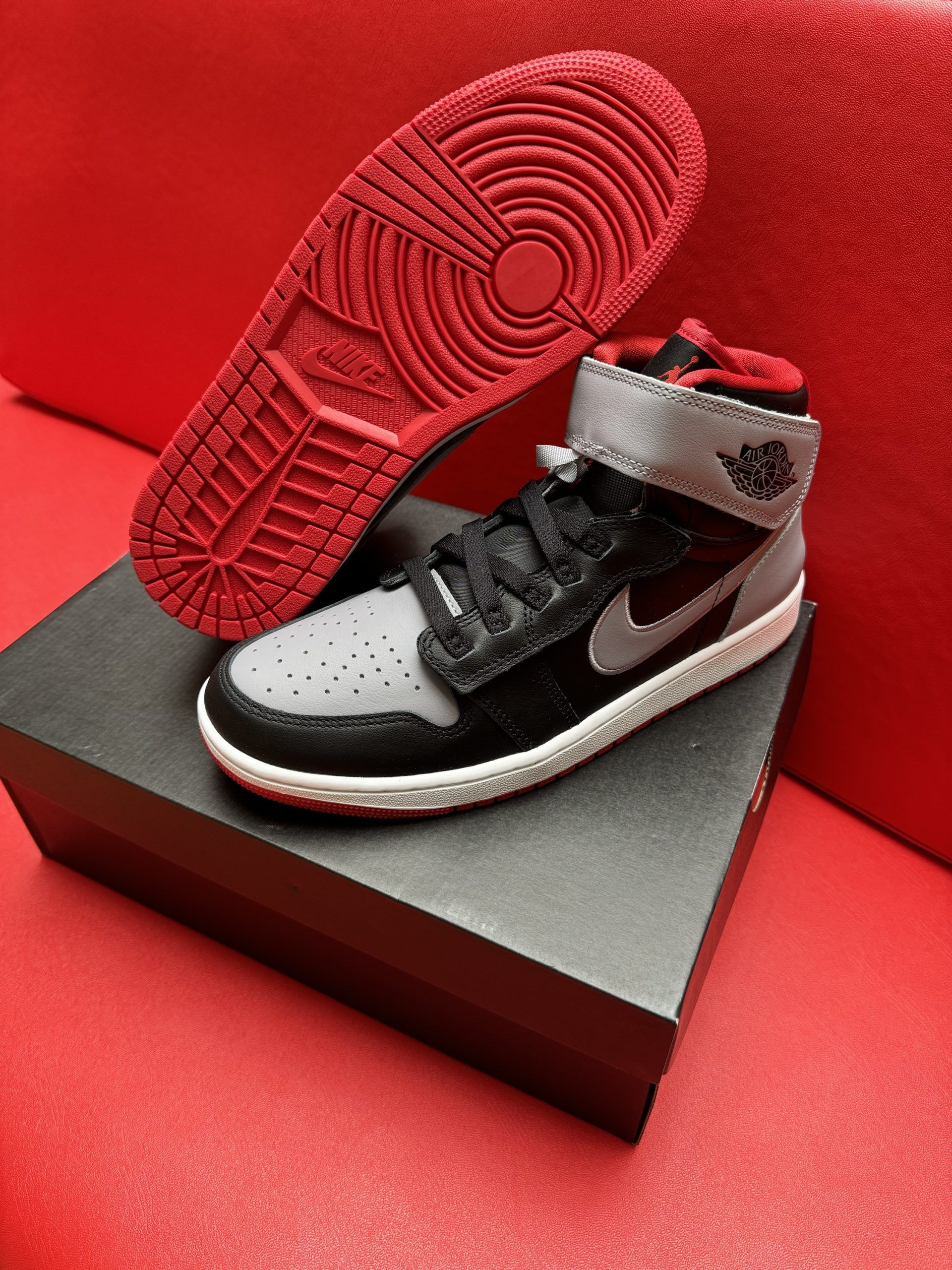Air Jordan 1 sneaker on a black box, with a red sole next to it, set against a red background.