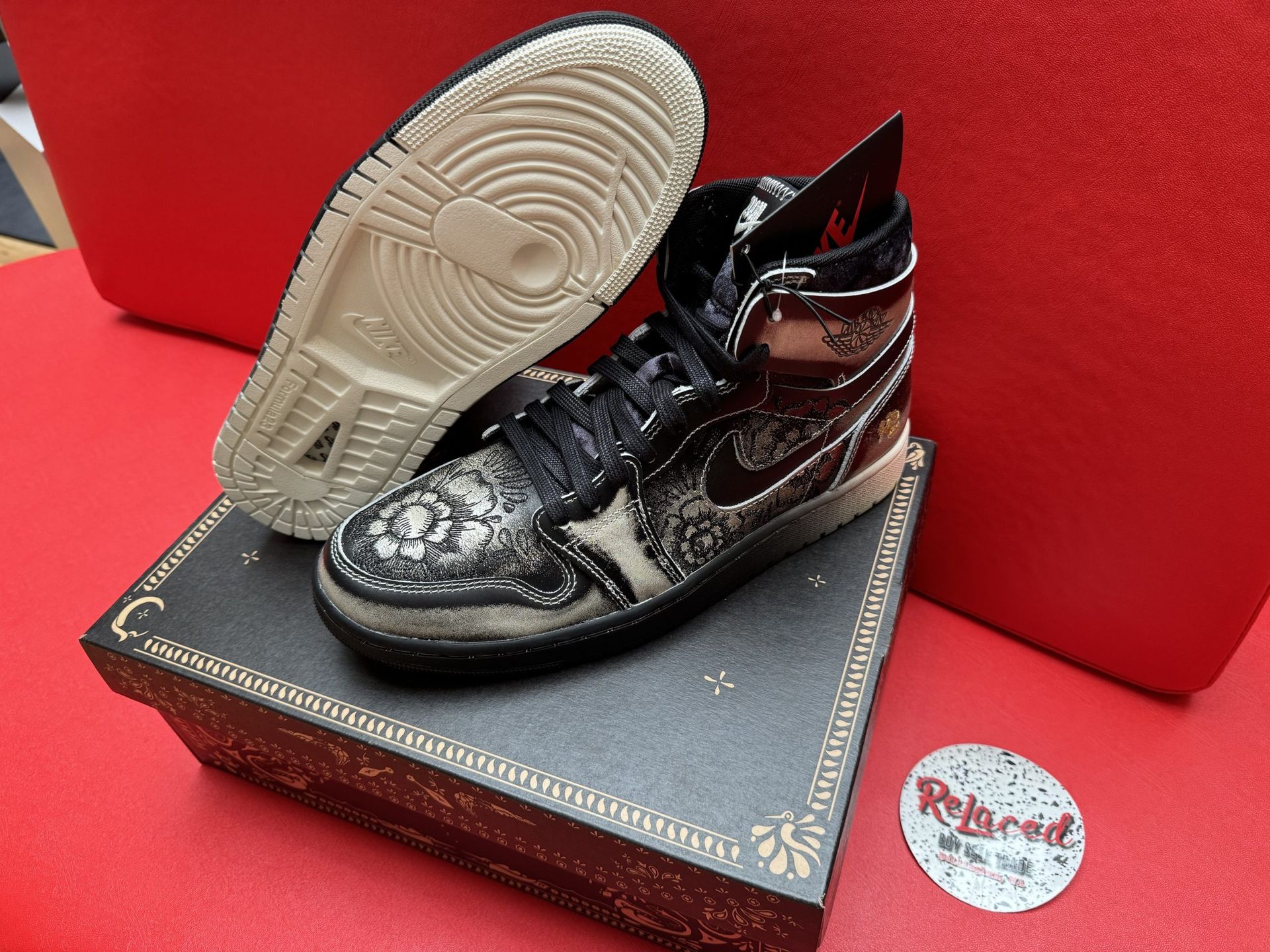 Black and white high-top sneaker with intricate floral pattern on a patterned box. Tan sole.