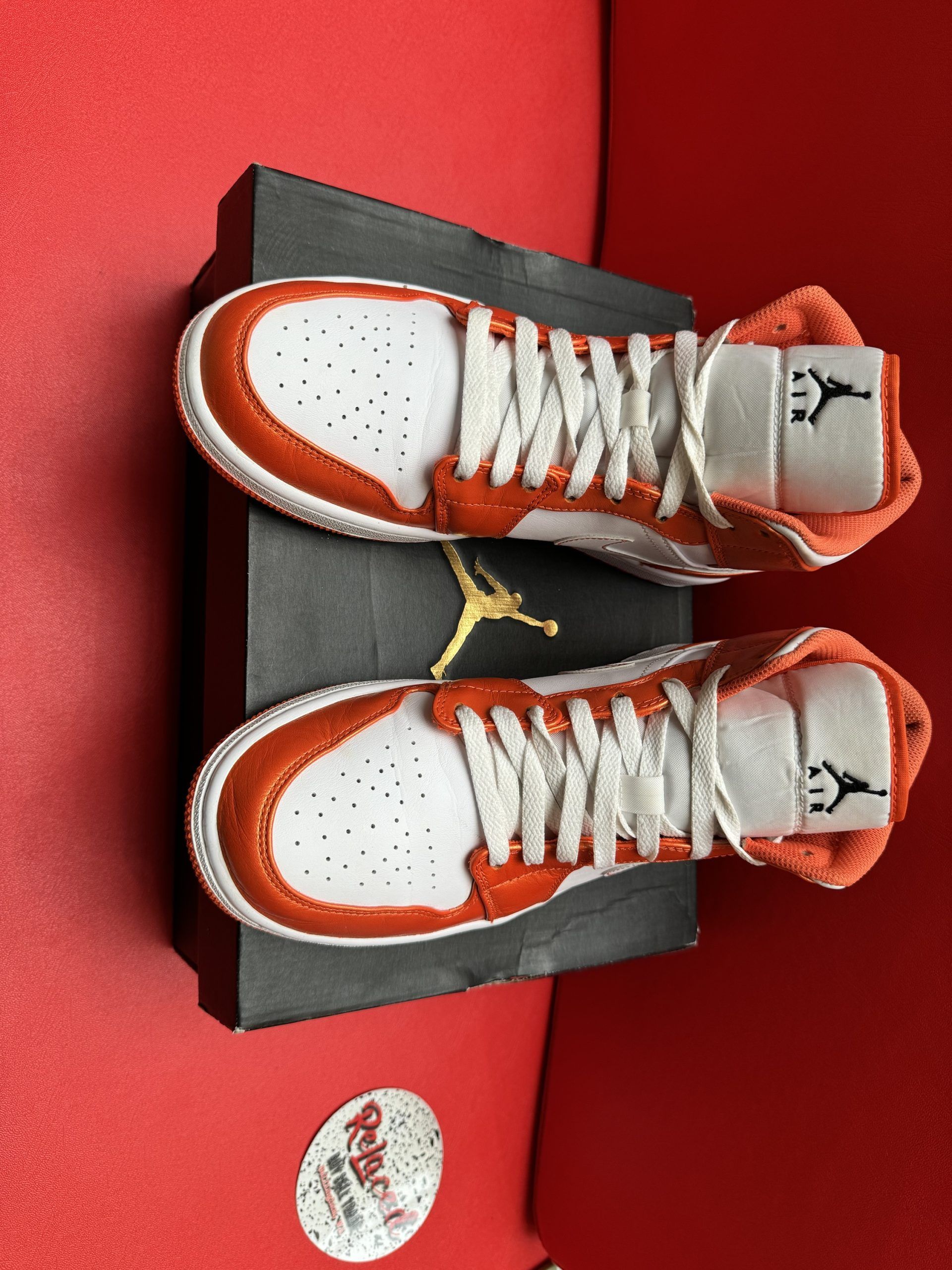 Orange and white Air Jordan sneakers on a black shoe box, set against a red background.