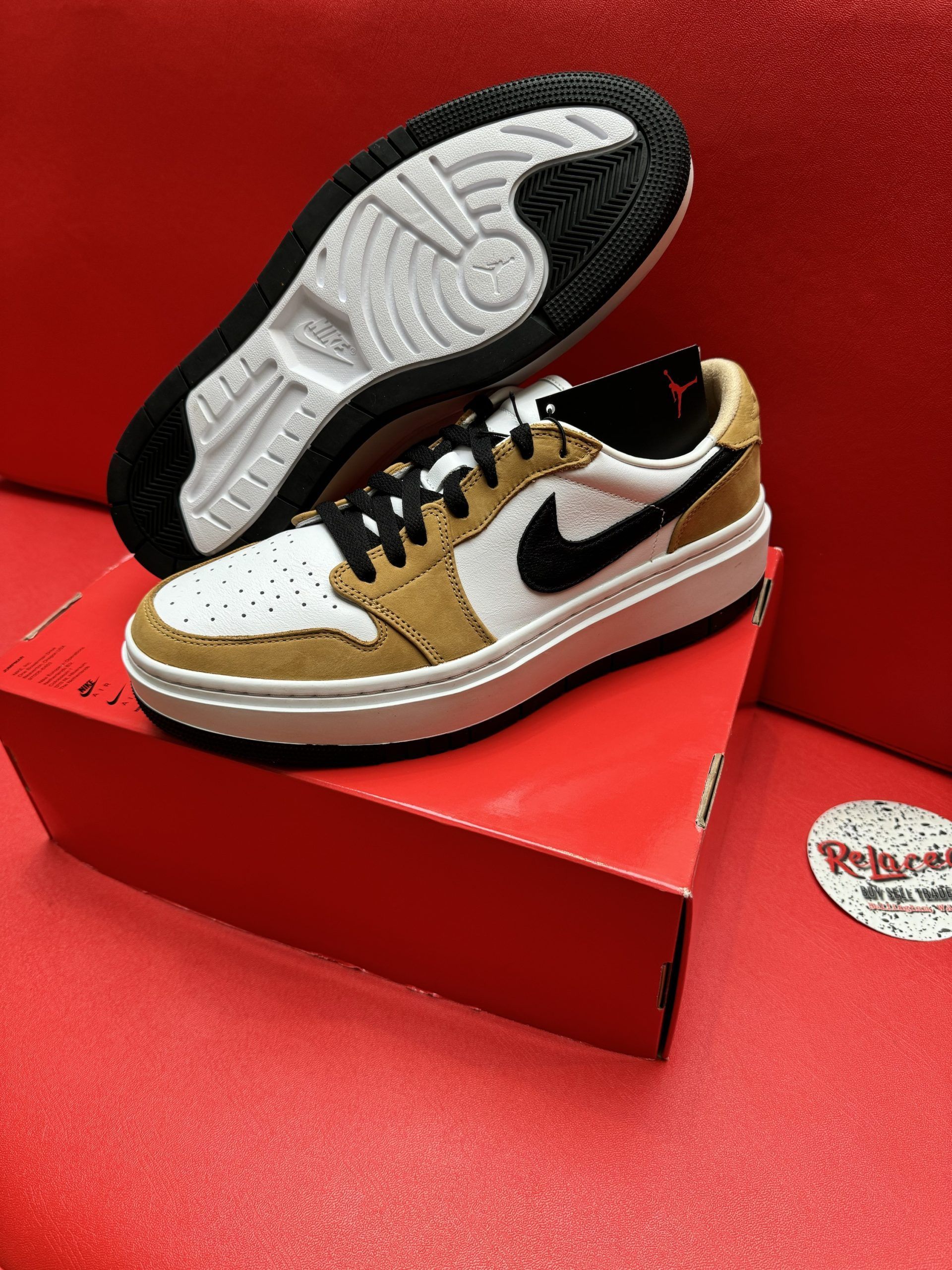 Pair of tan, white, and black Jordan sneakers on a red box; sole is visible.