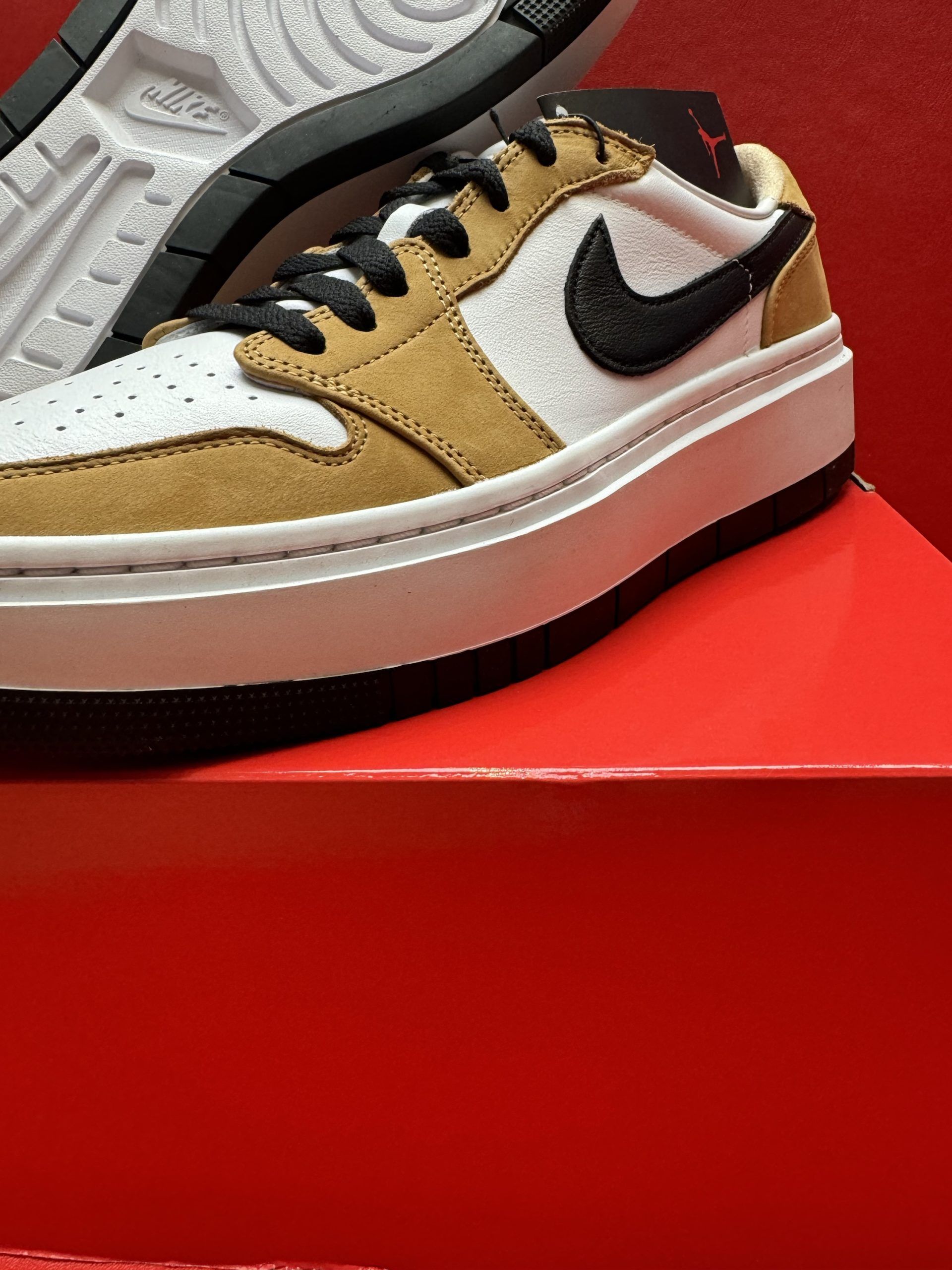 Pair of tan, white, and black Jordan sneakers on a red box; sole is visible.