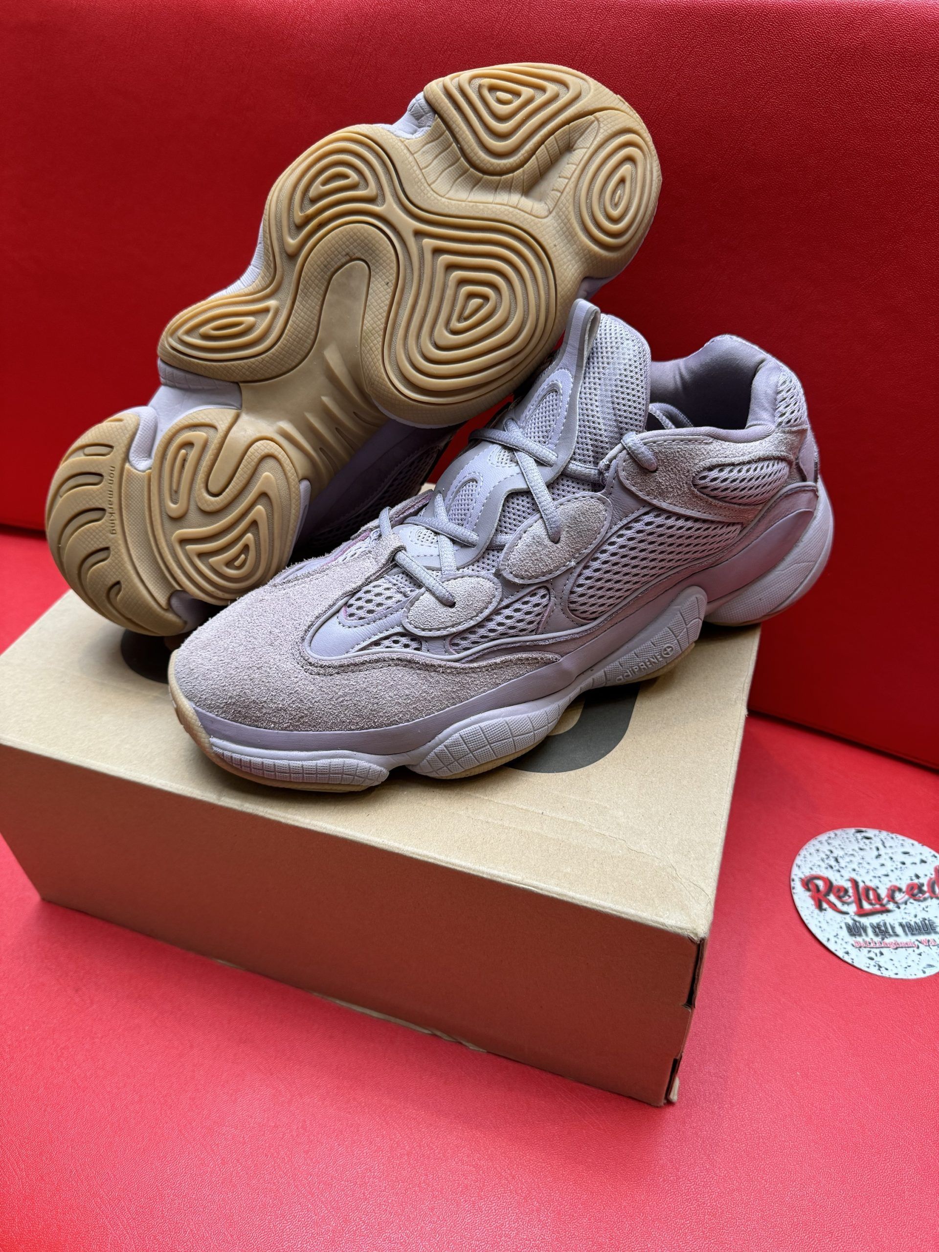 Yeezy 500 sneakers, light purple, on a box and a red surface. The sole of one is visible.