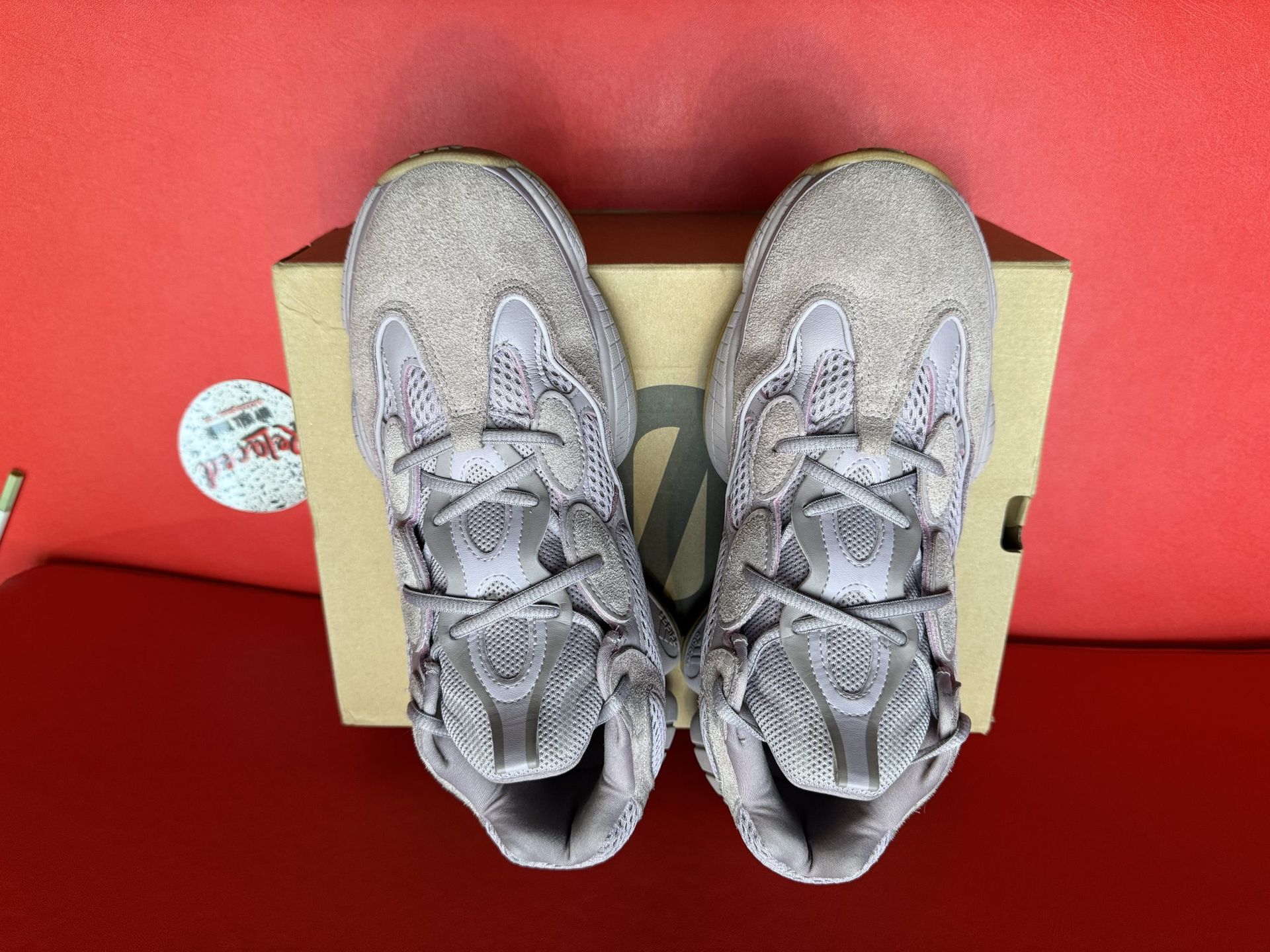 Yeezy 500 sneakers, light purple, on a box and a red surface. The sole of one is visible.