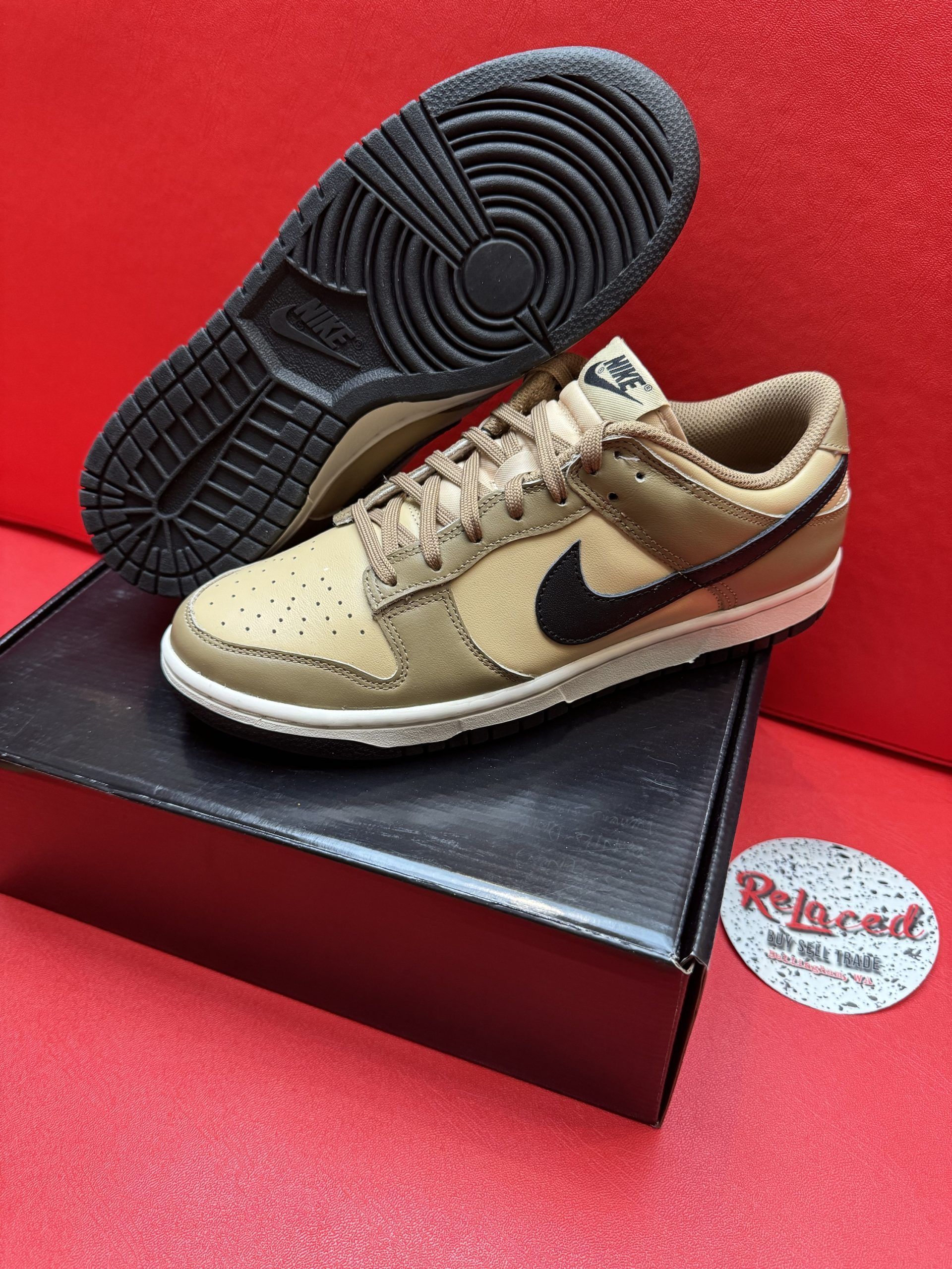 Brown Nike Dunk Low sneakers with black swoosh and sole, on a black box, red background.