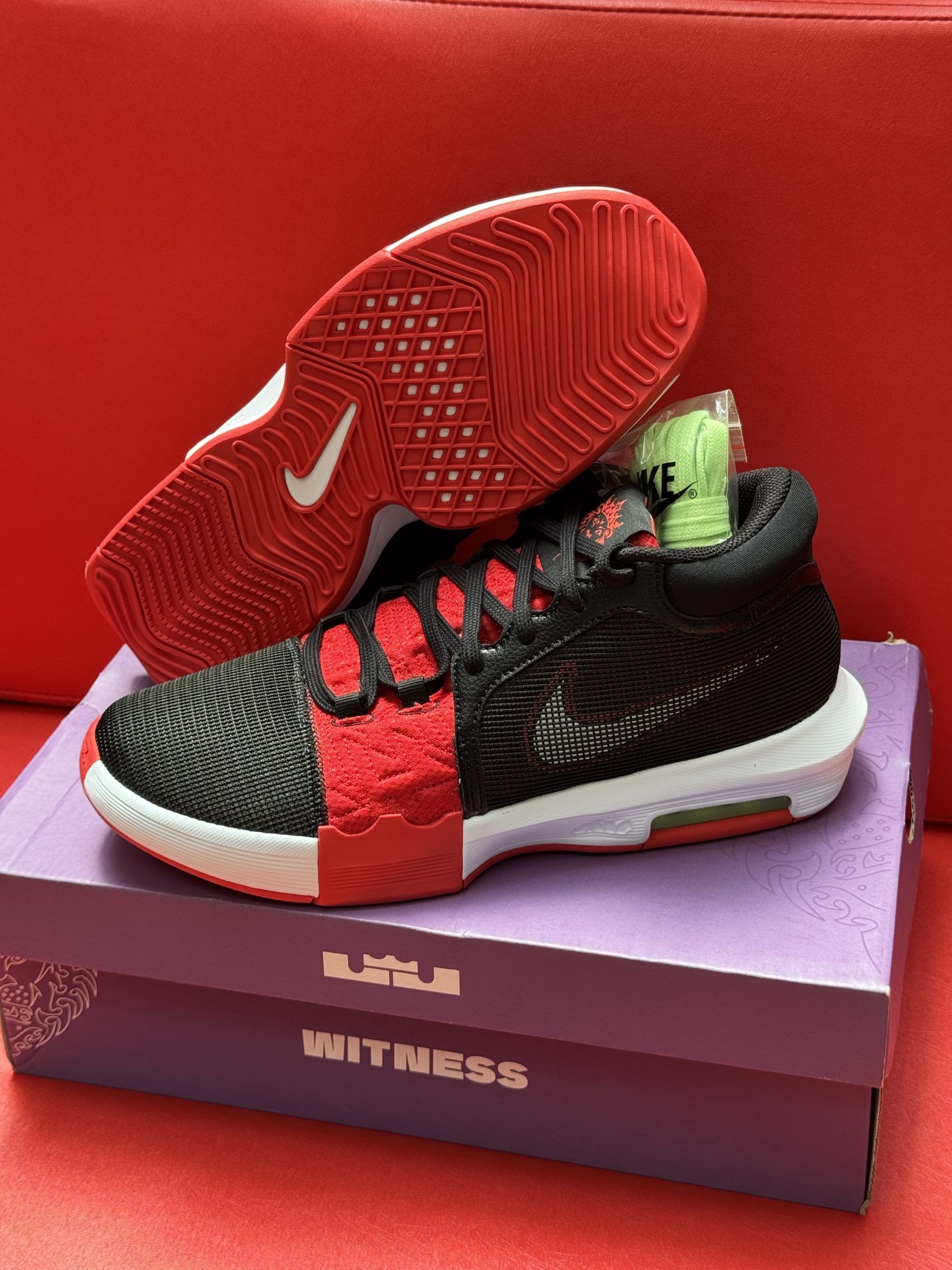 Black and red Nike LeBron Witness basketball shoe on a purple shoe box, red sole visible.