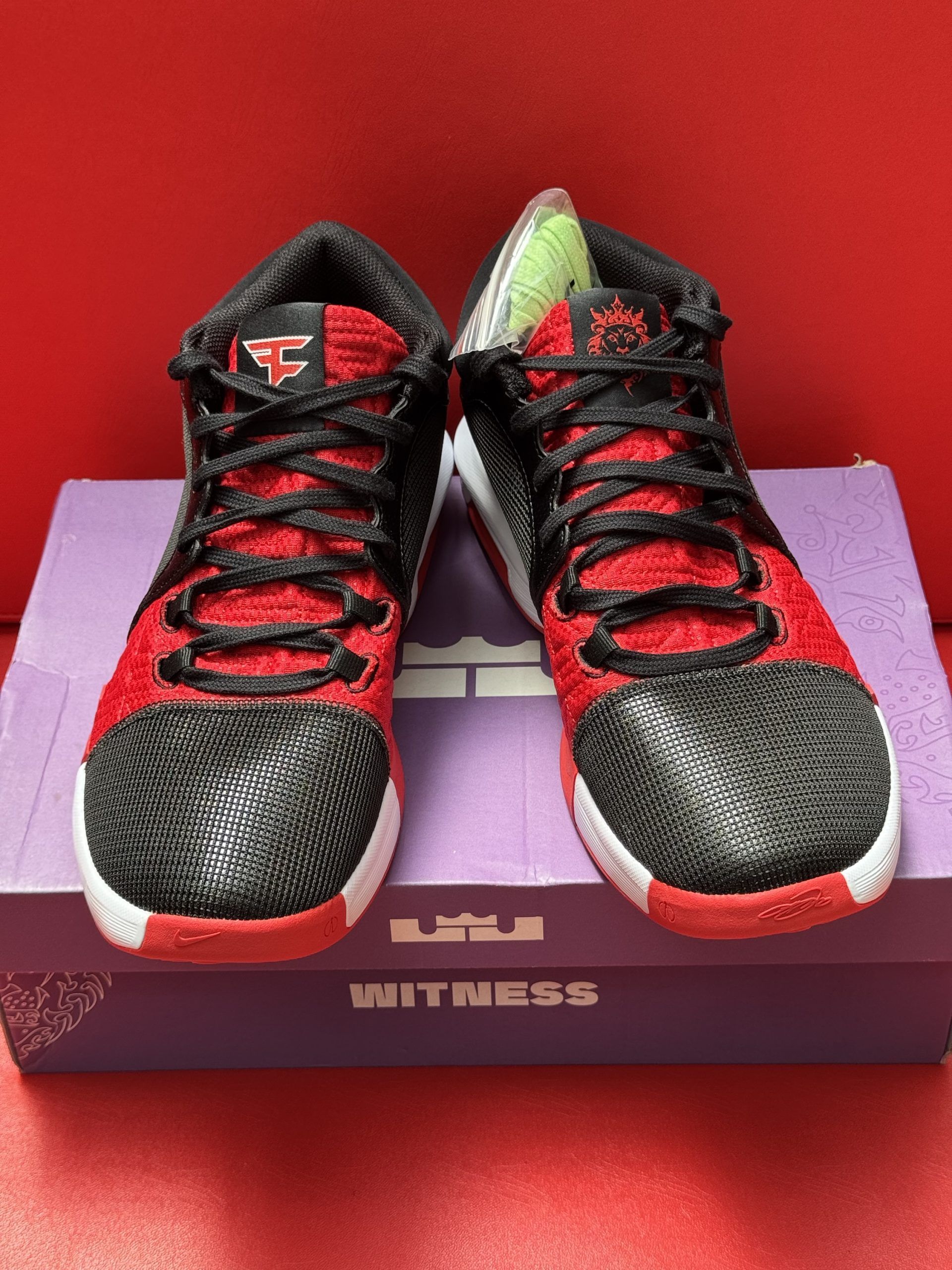 Black and red Nike LeBron Witness basketball shoe on a purple shoe box, red sole visible.