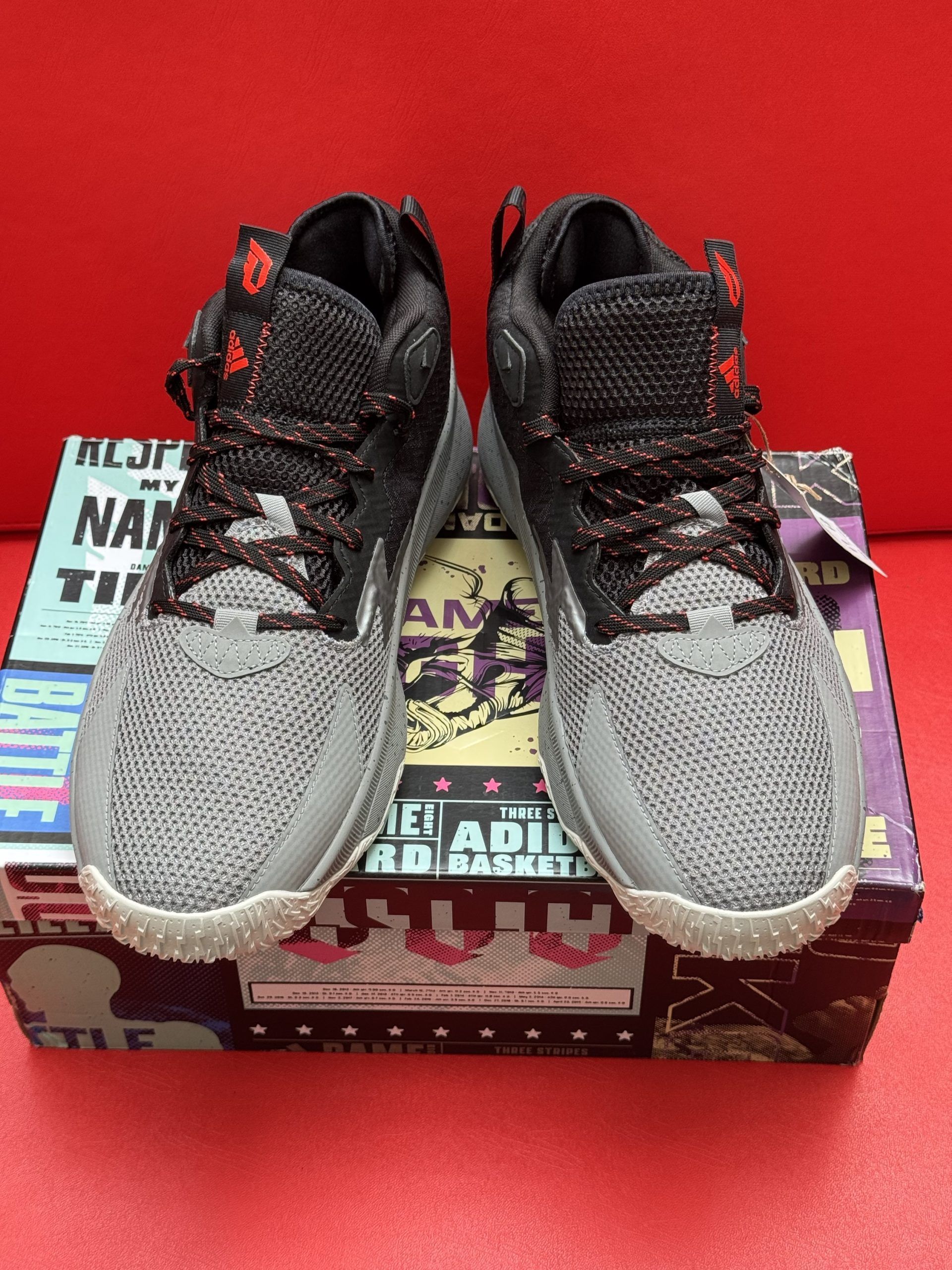 Gray and black Adidas basketball shoes with a price tag, sitting on a colorful shoebox.