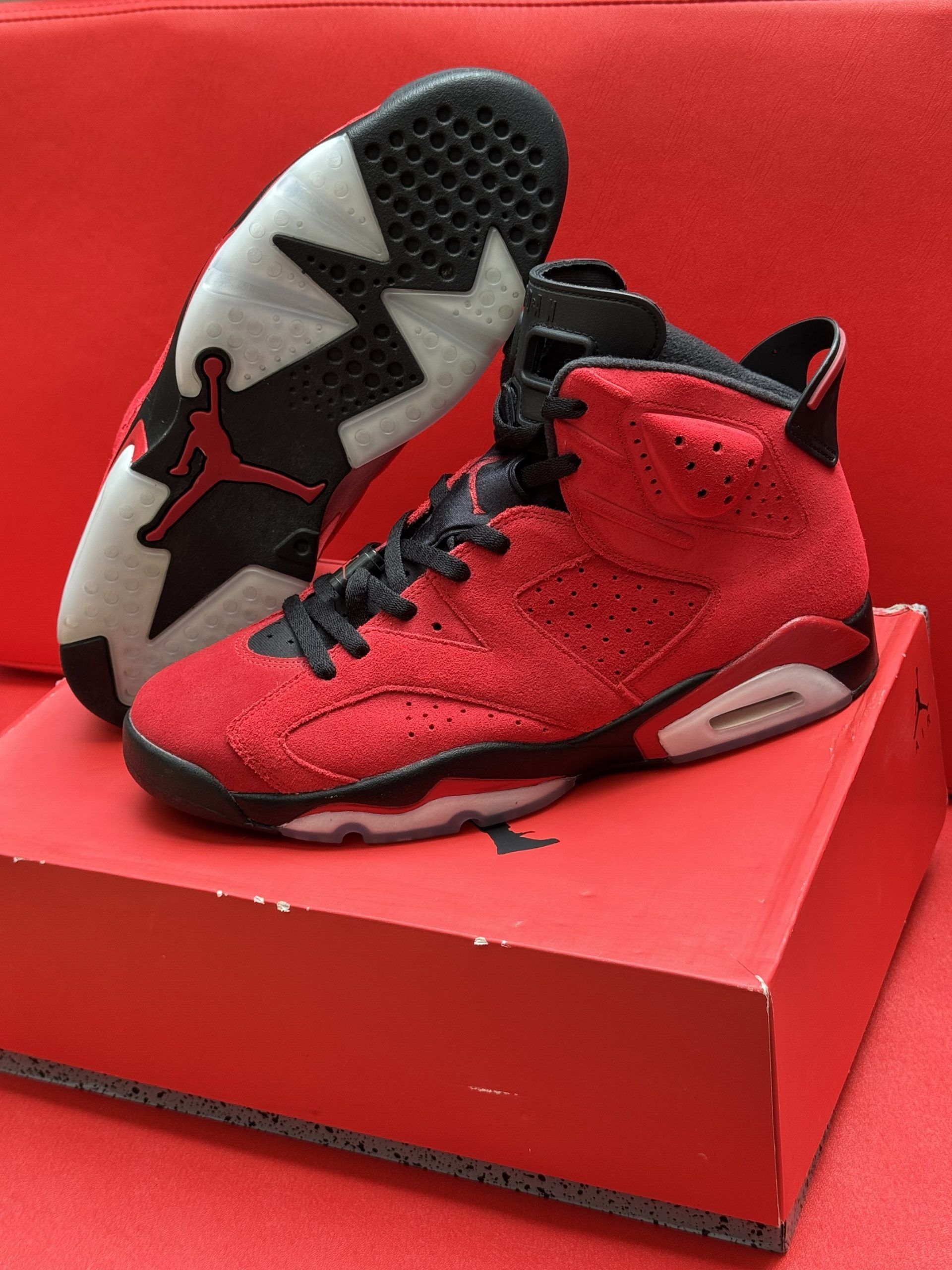 Red and black Air Jordan 6 sneakers on a red shoe box, with the sole visible, showing a black and white design.