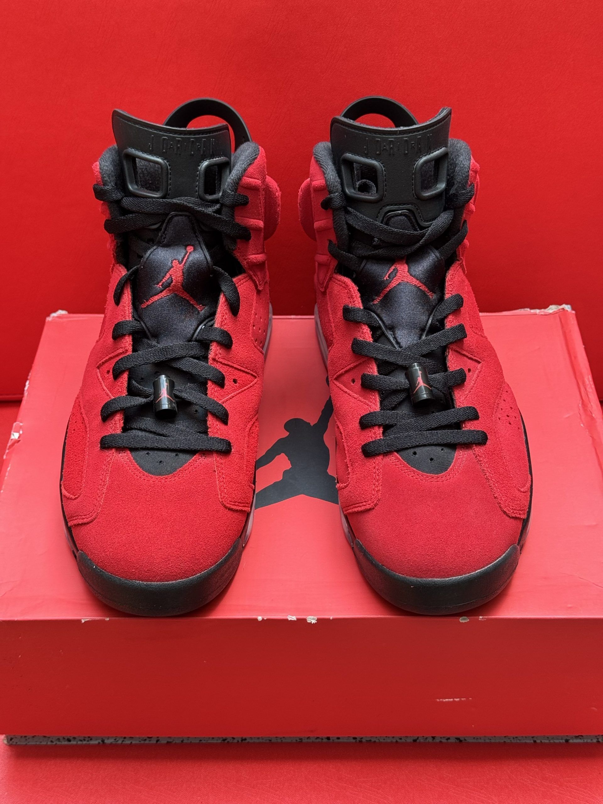 Red and black Air Jordan 6 sneakers on a red shoe box, with the sole visible, showing a black and white design.