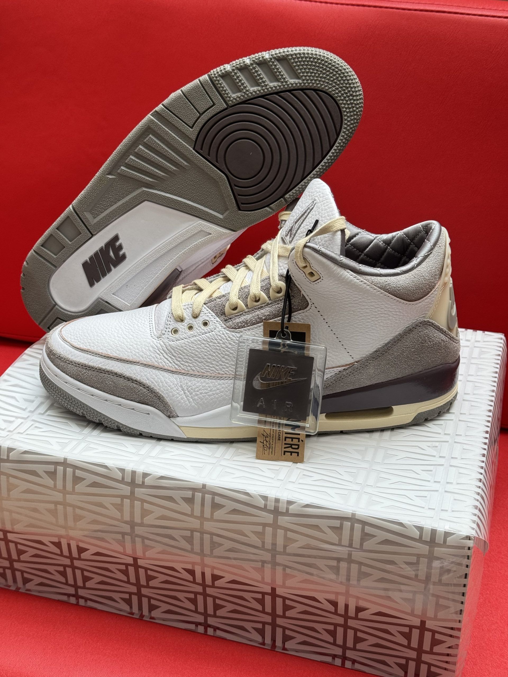 Air Jordan 3 sneakers on a patterned box. White, grey, and brown colors. One shoe's sole is visible.