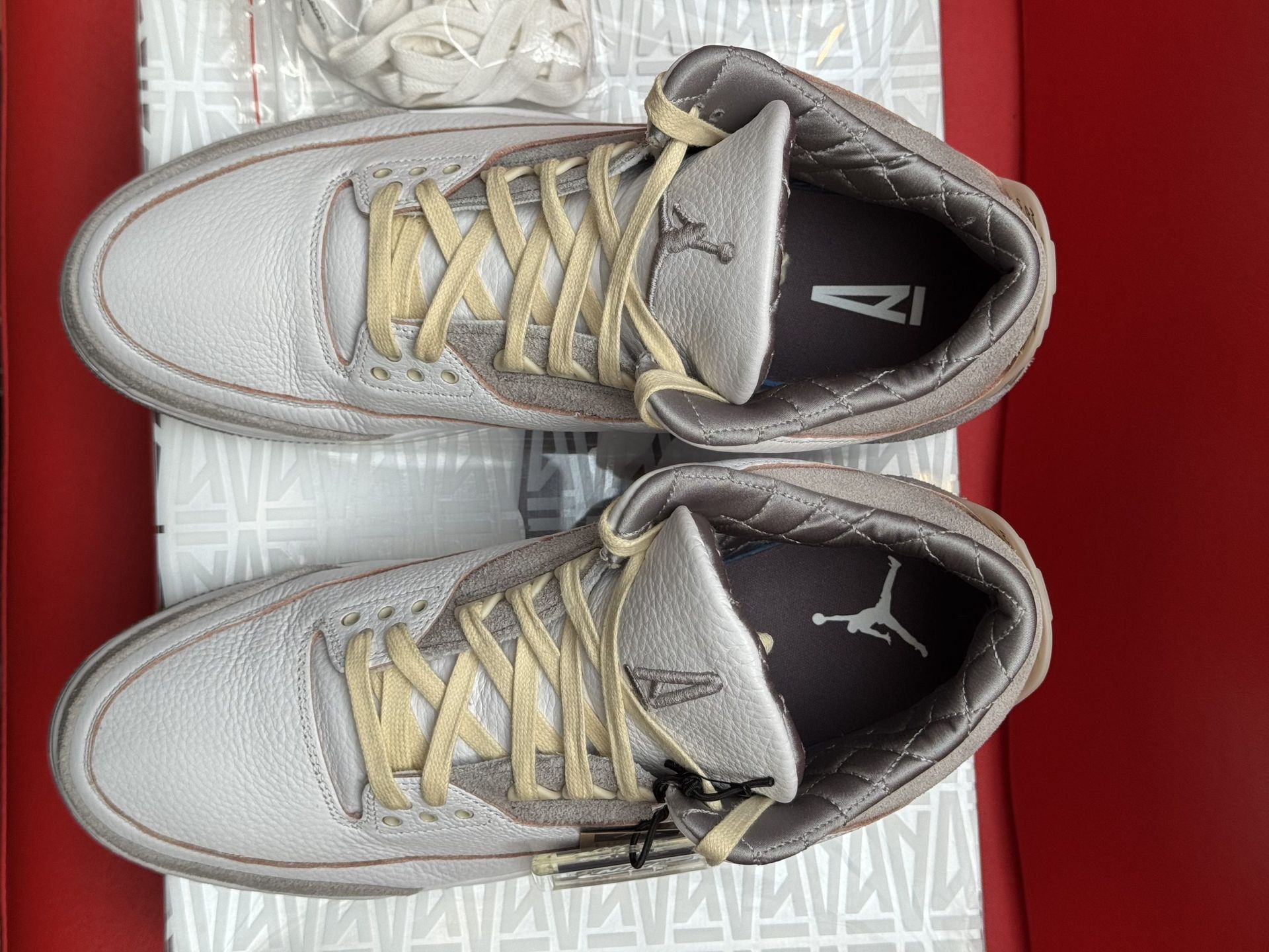 Air Jordan 3 sneakers on a patterned box. White, grey, and brown colors. One shoe's sole is visible.