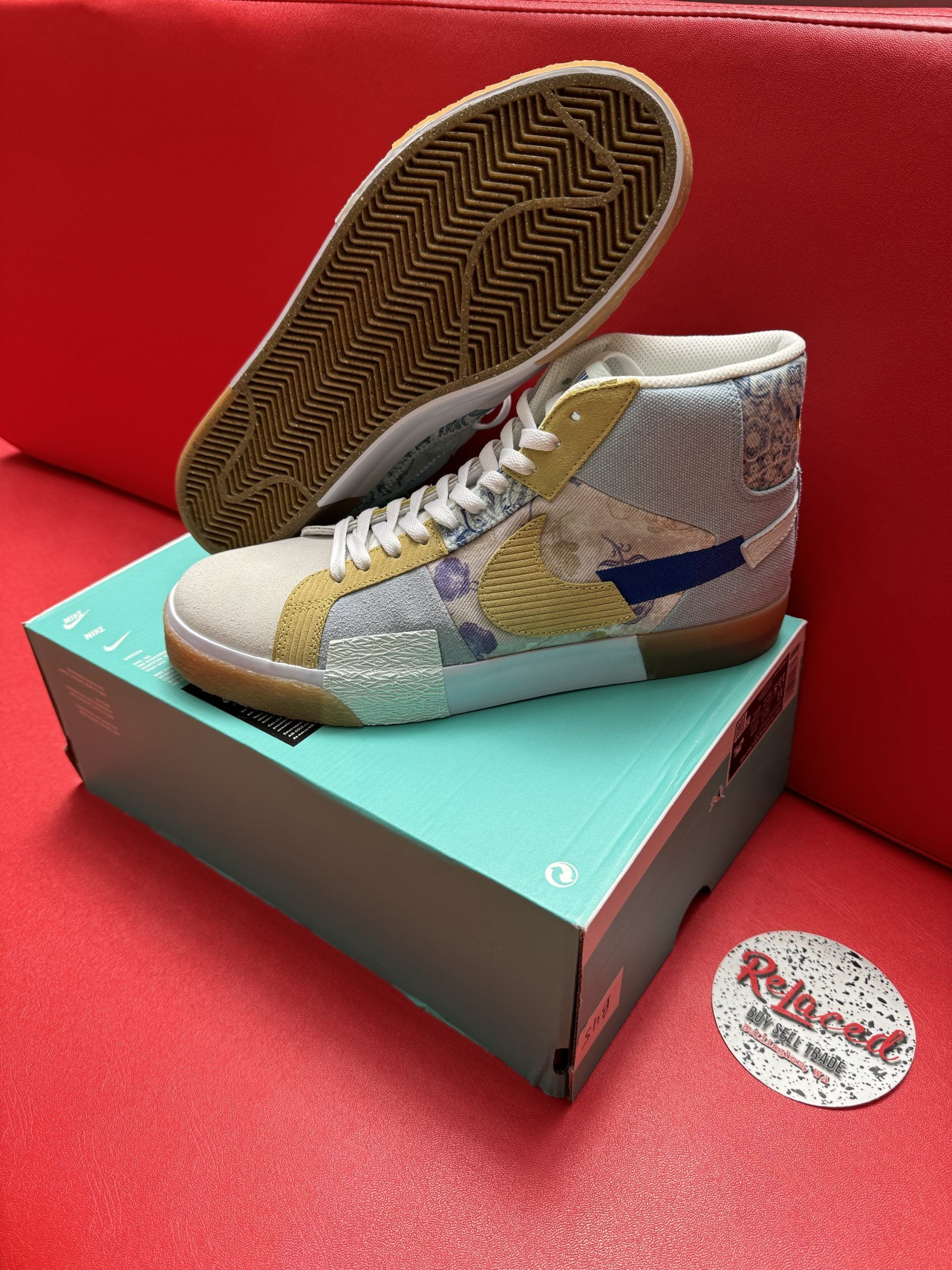 High-top, patchwork sneakers on a teal shoe box. One shoe is off the box, showing a gum-colored sole. Red background.