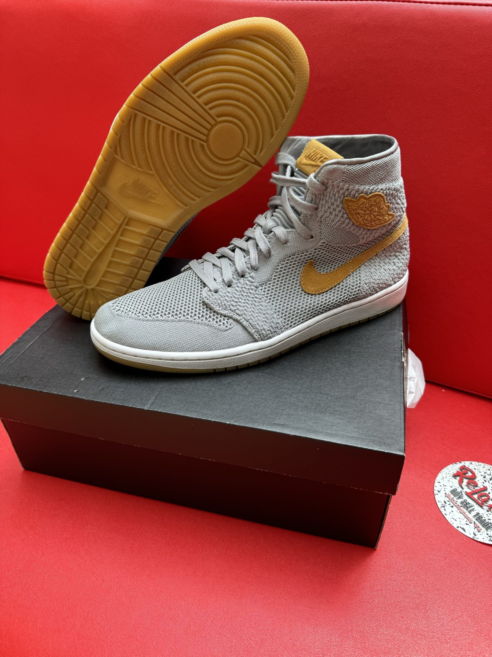 Gray and gold high-top sneaker on a black box, with a separate tan sole visible, set against a red background.
