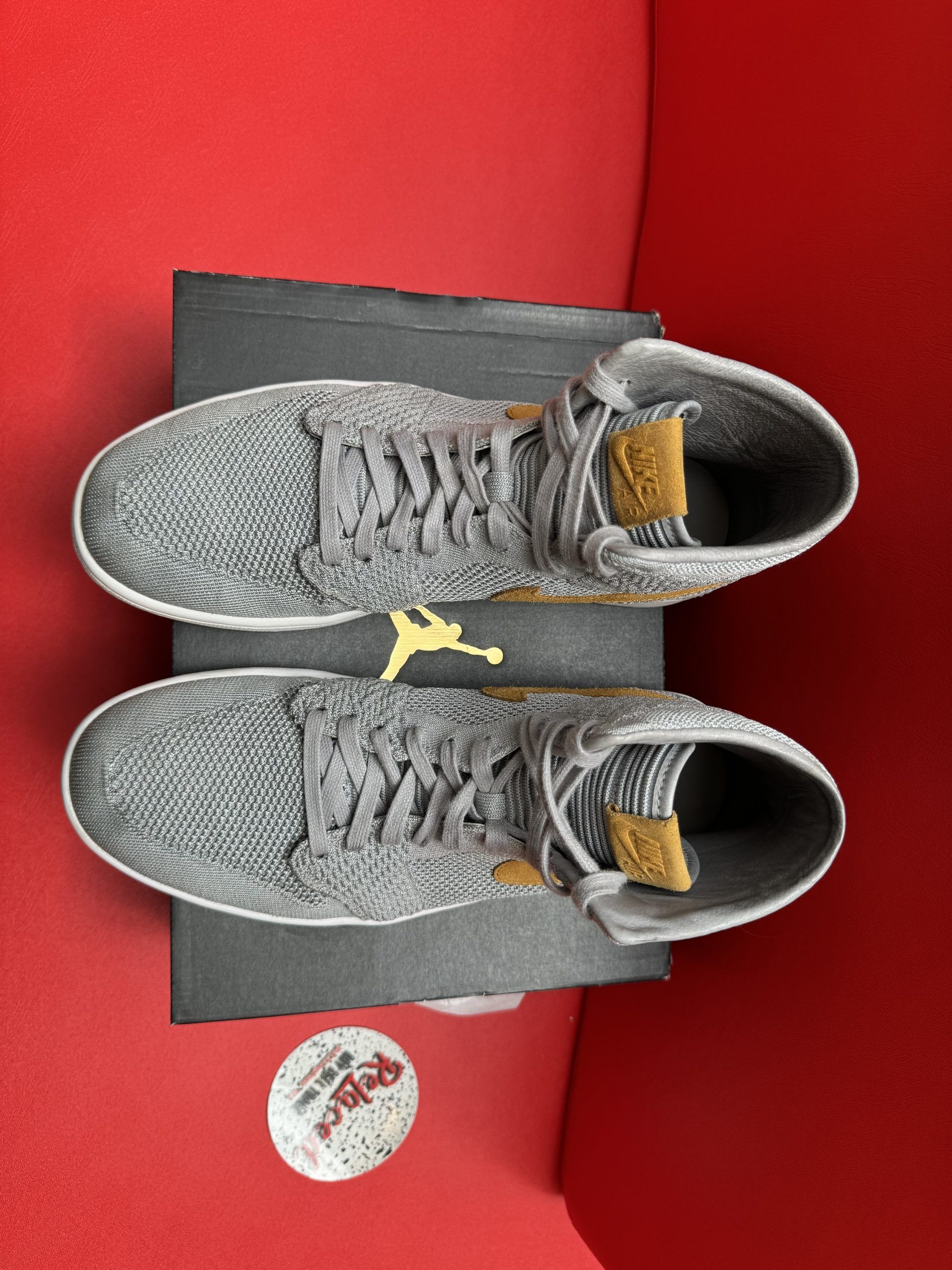 Gray and gold high-top sneaker on a black box, with a separate tan sole visible, set against a red background.