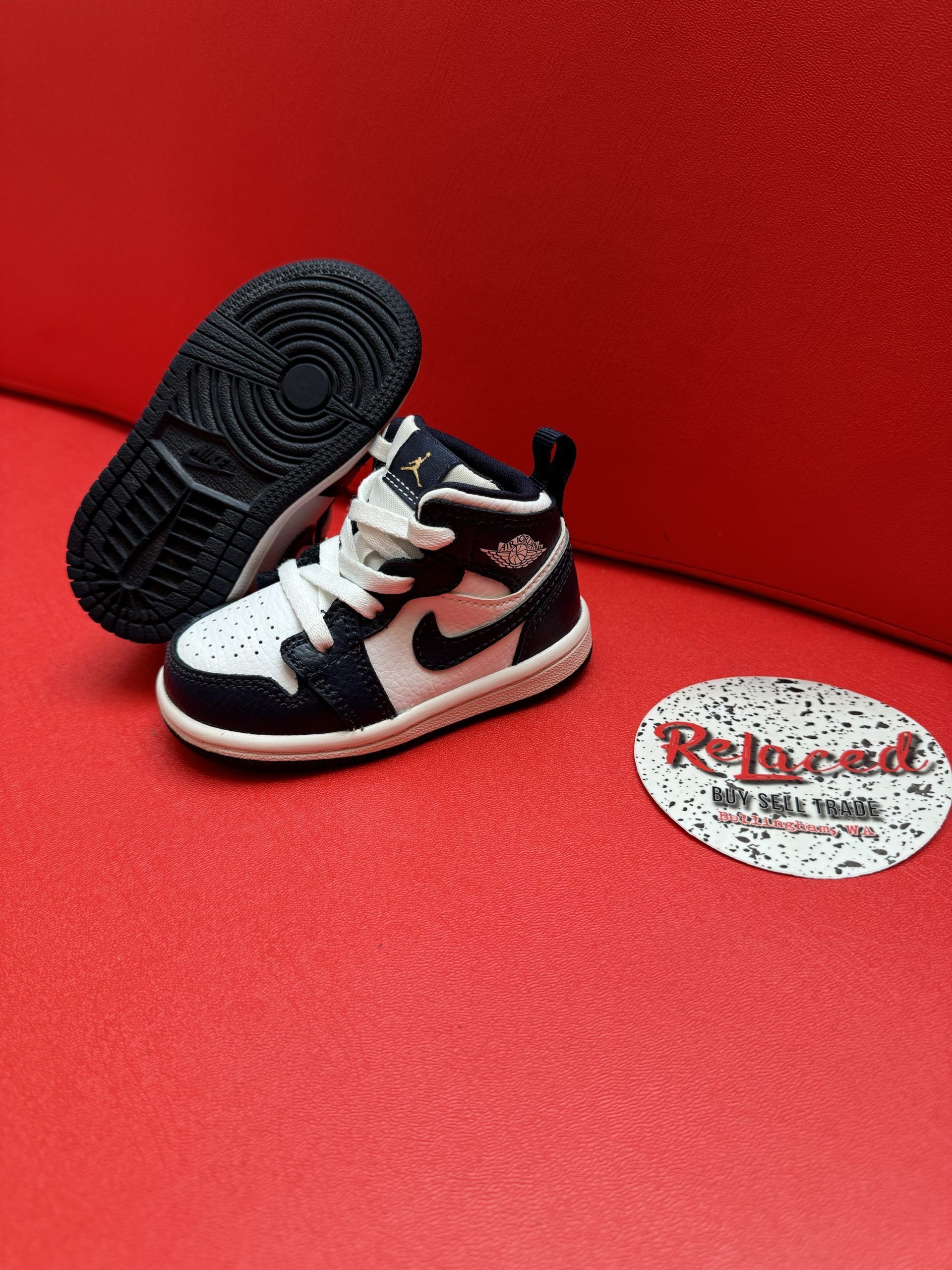 Pair of black and white toddler Air Jordan 1 sneakers on a red surface.