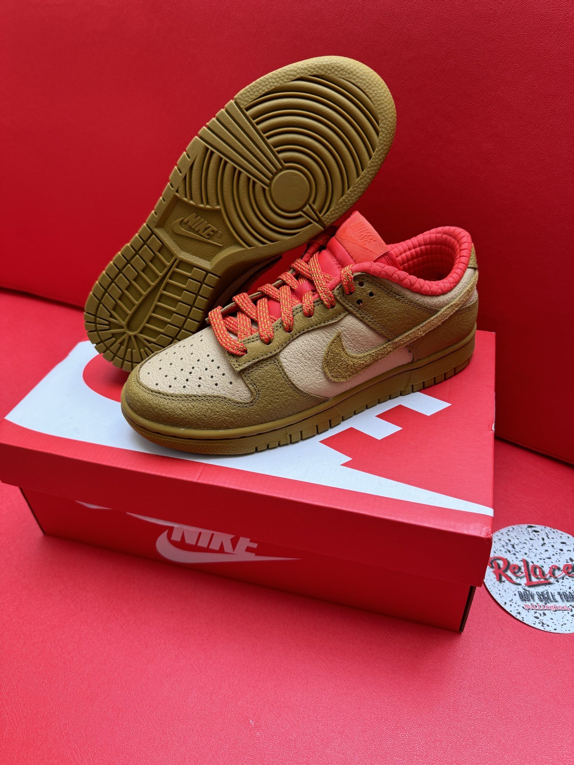 Brown and tan Nike Dunk Low sneakers with textured uppers, resting on a red Nike box, with a red background.