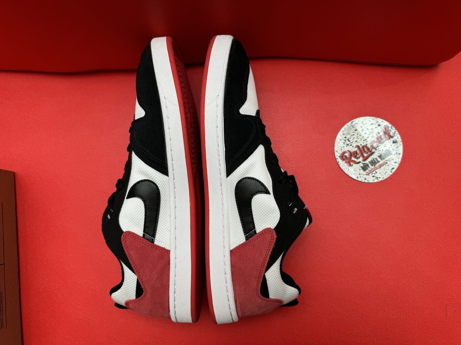 Nike skate shoe, black and white with red accents, on a cardboard box against a red backdrop.