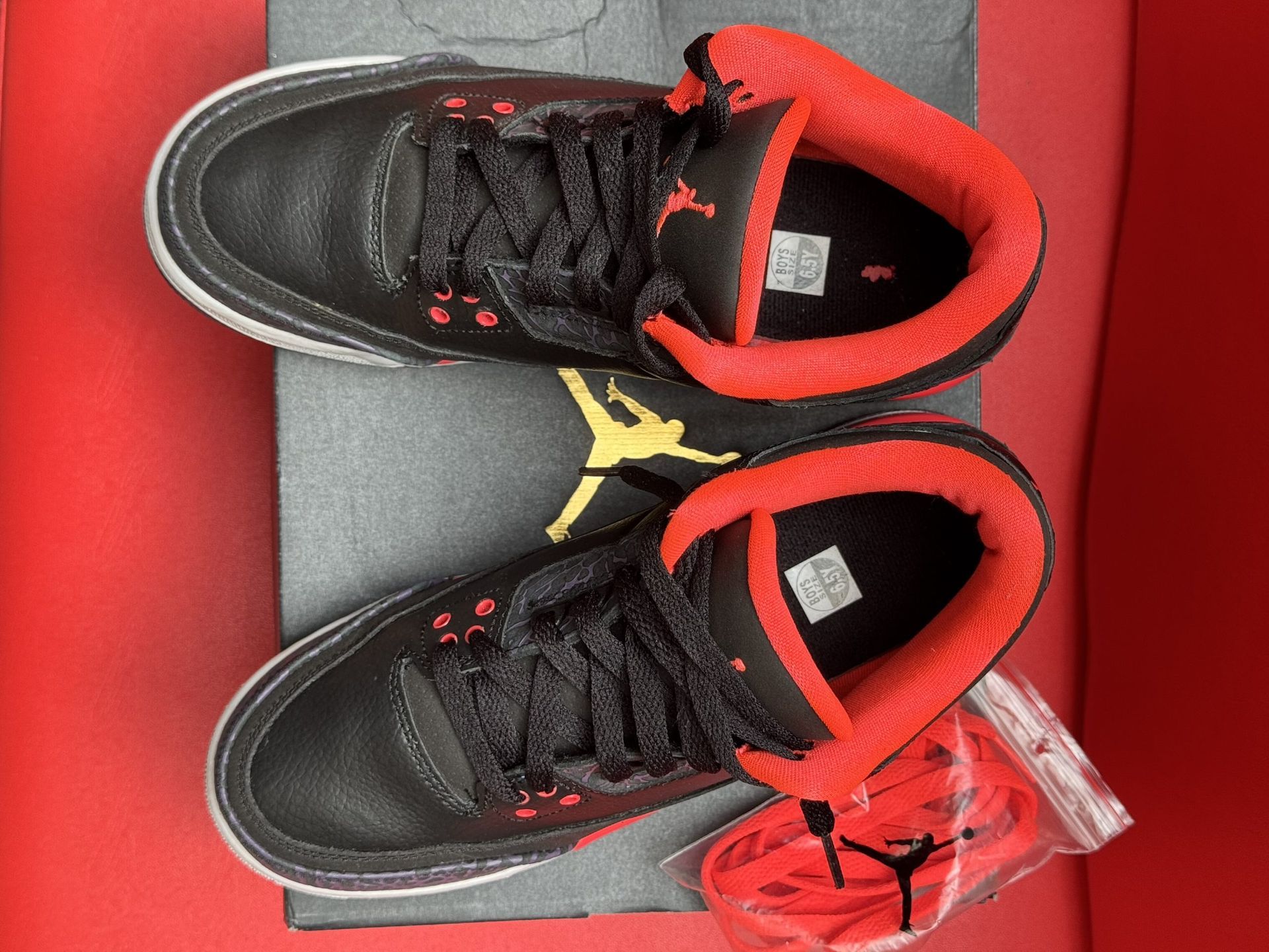 Black and red Air Jordan 3 sneakers on a box, with extra laces and a red sole.