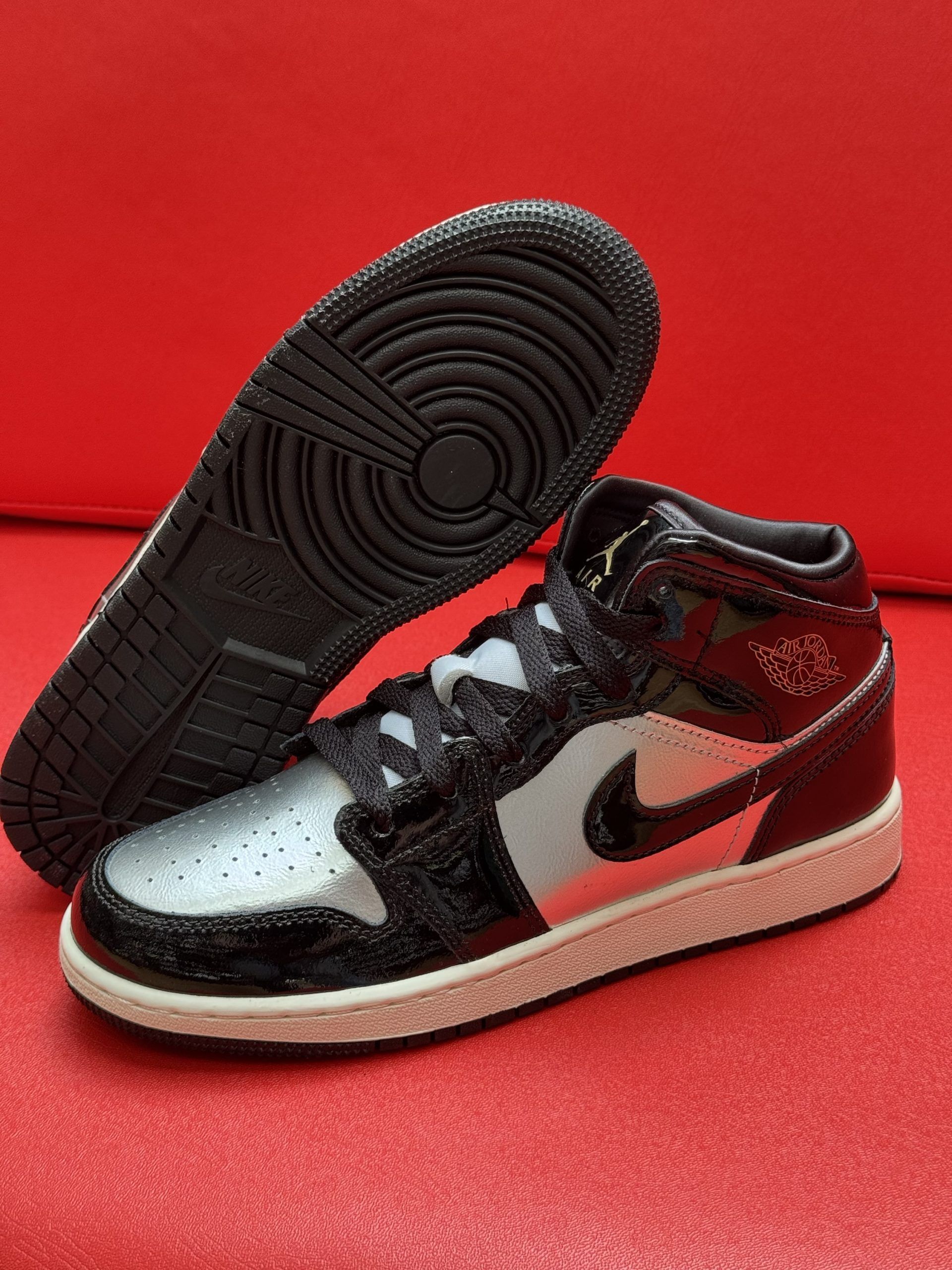 Black and silver Air Jordan 1 sneaker with a white sole, set on a red surface.