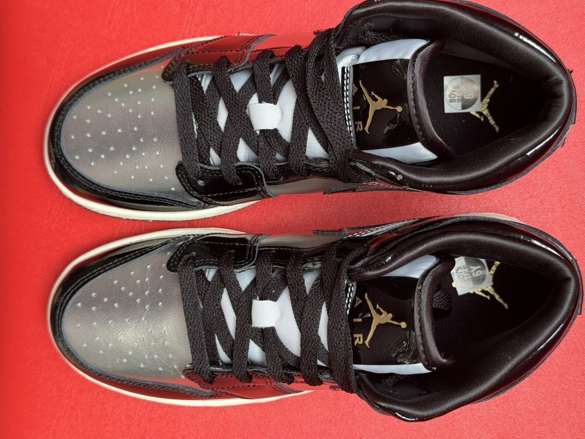 Black and silver Air Jordan 1 sneaker with a white sole, set on a red surface.