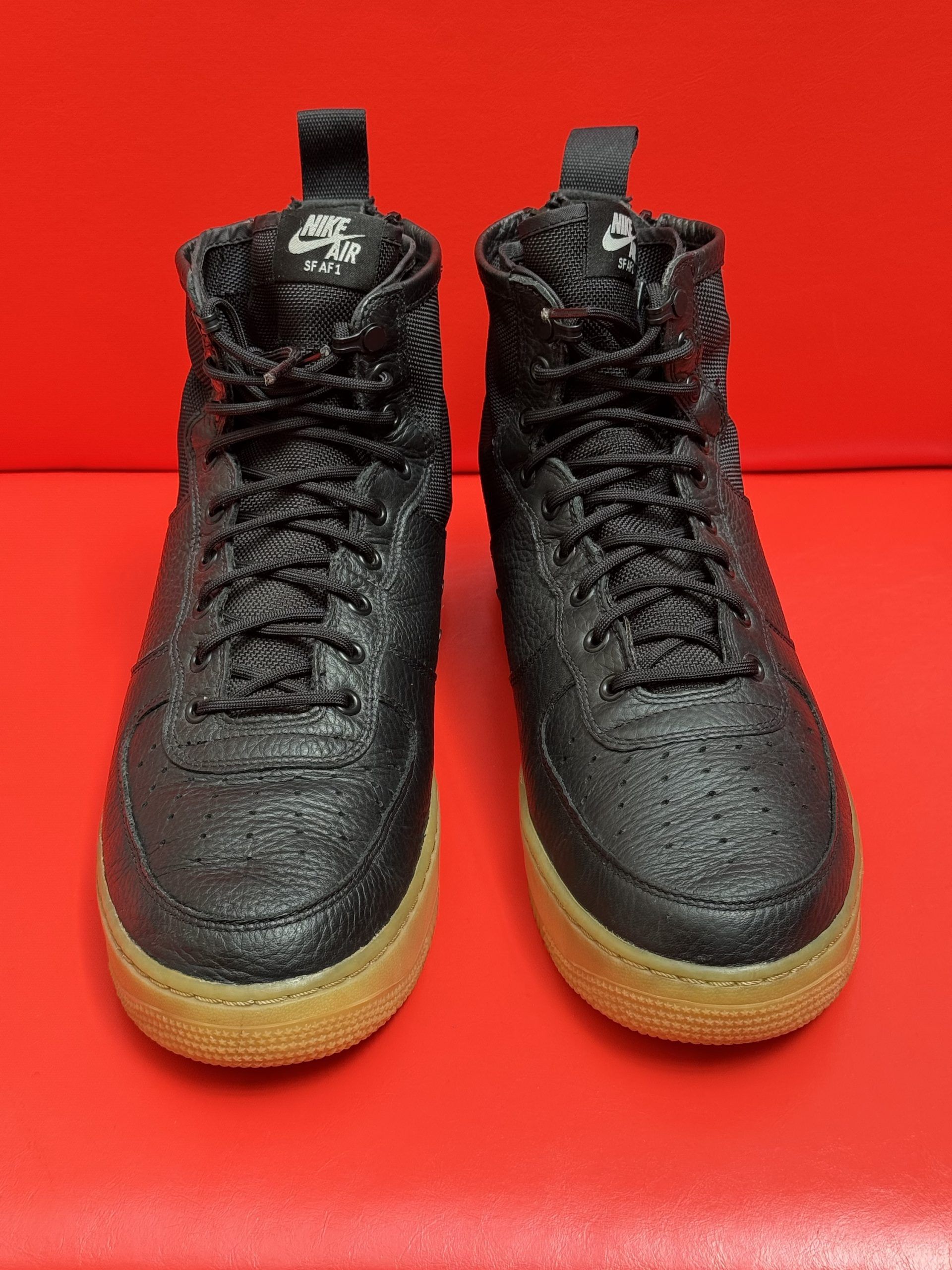 Black high-top sneakers with textured uppers, brown soles, and a red background. One shoe is flipped over to show the sole.