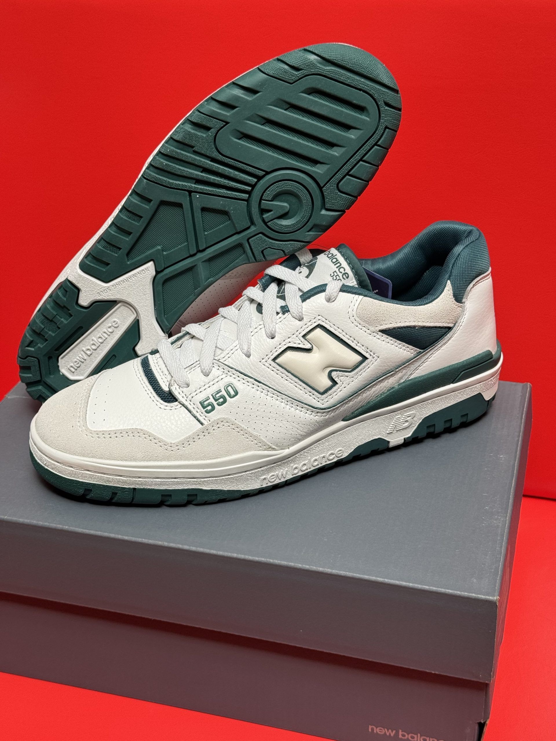 New Balance 550 sneakers, white leather, green accents, sitting atop a gray shoebox. Green sole visible.